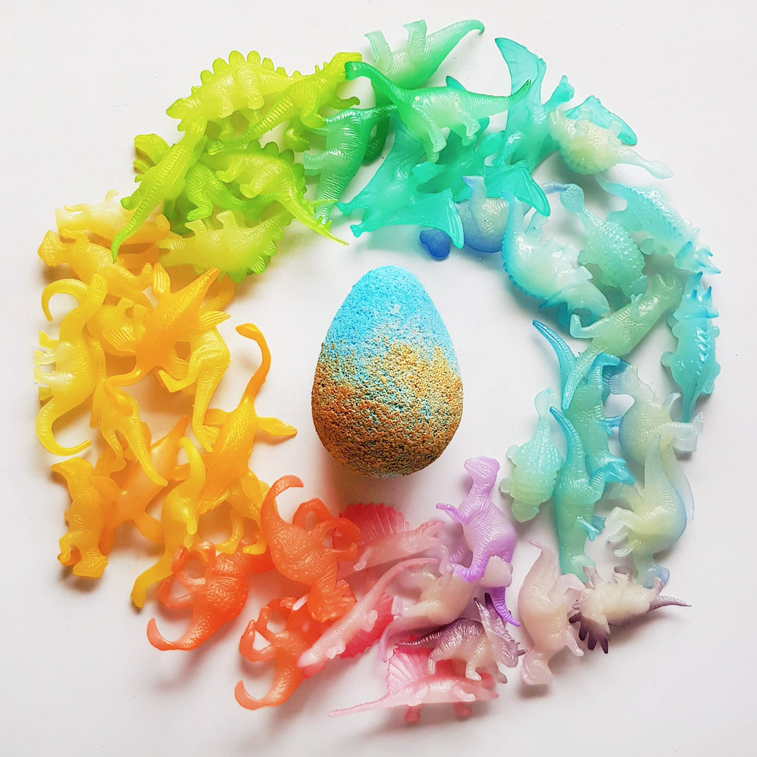 Rainbow arrangement of dinosaur toys around a surprise egg bath bomb