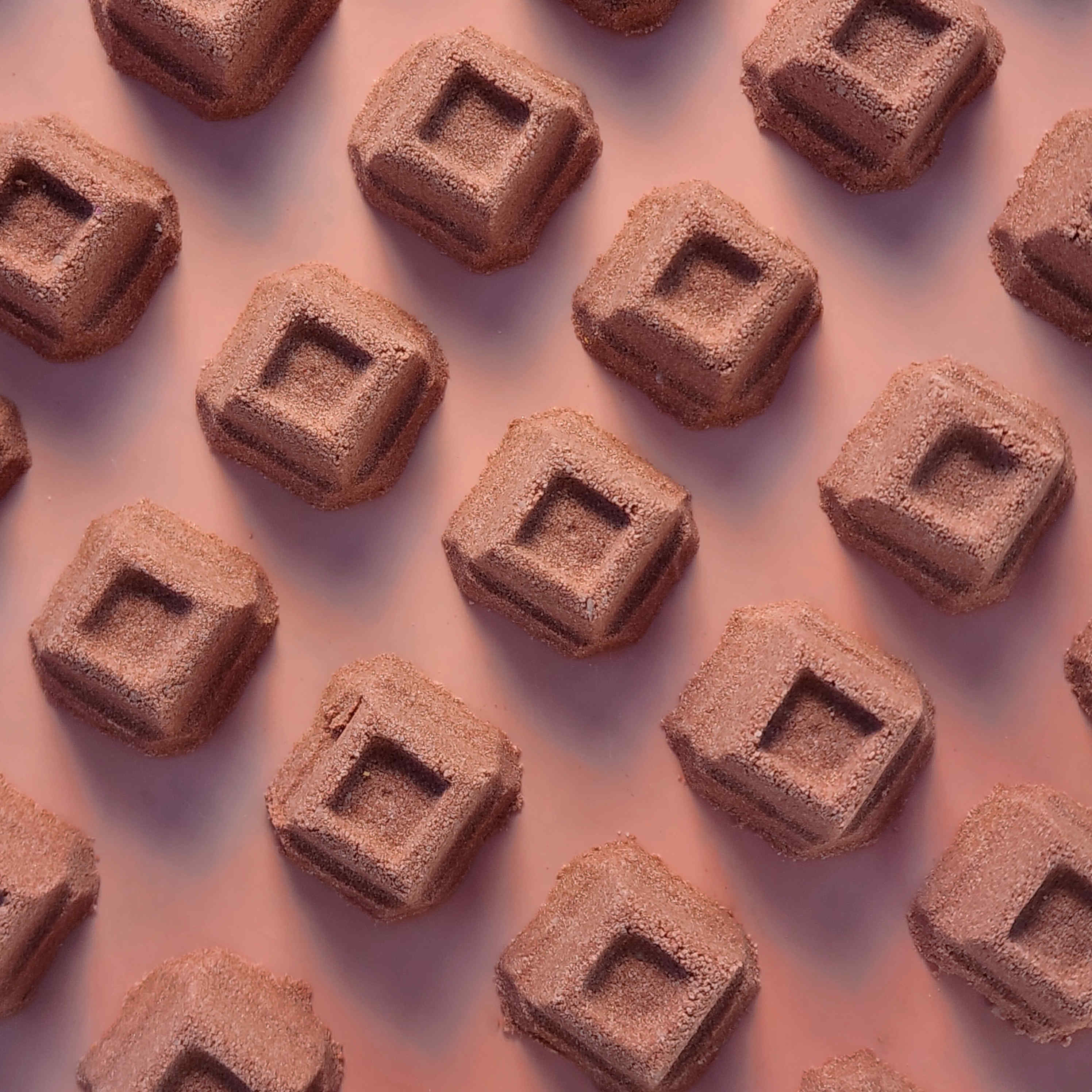Chocolate square mini bath bombs arranged on a pink background