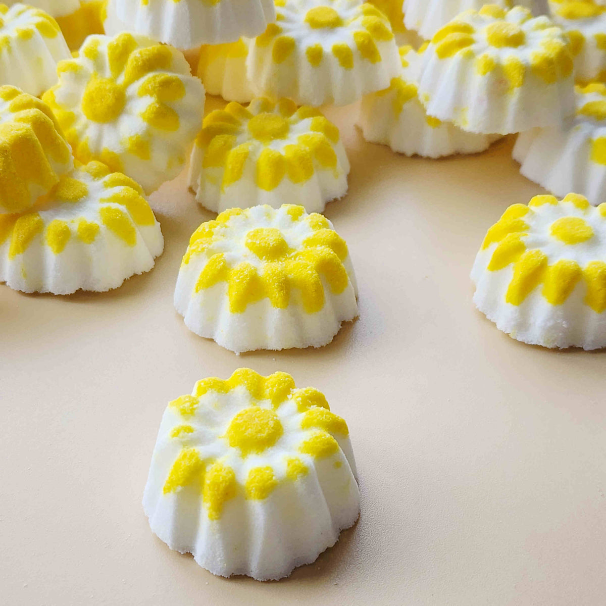 chamomile shaped mini bath bombs with a white base and yellow detail on a neutral plain background