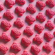 Red frog gummy candy shaped bath bombs layed out in an array over a plain red background