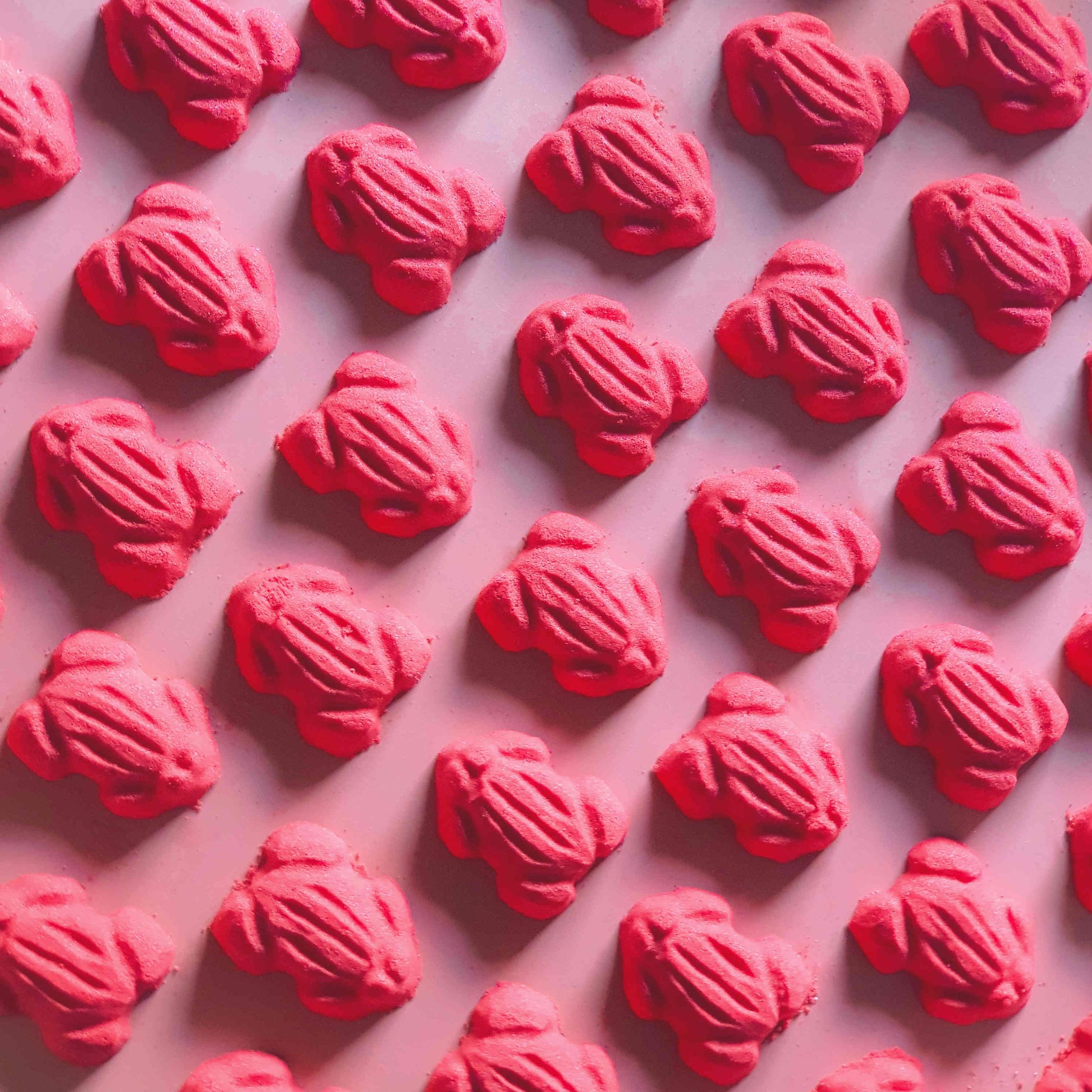 Red frog gummy candy shaped bath bombs layed out in an array over a plain red background