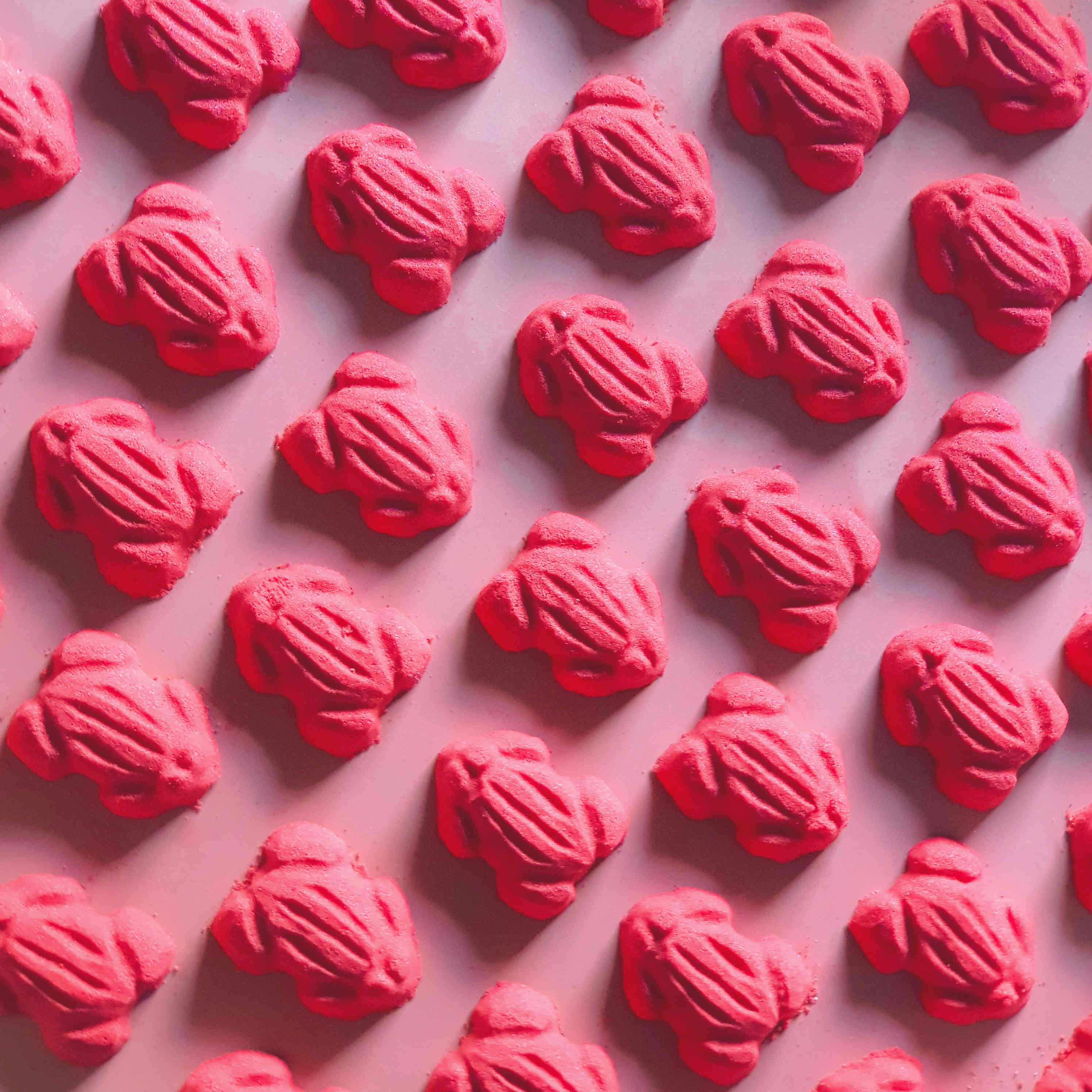 Red frog gummy candy shaped bath bombs layed out in an array over a plain red background