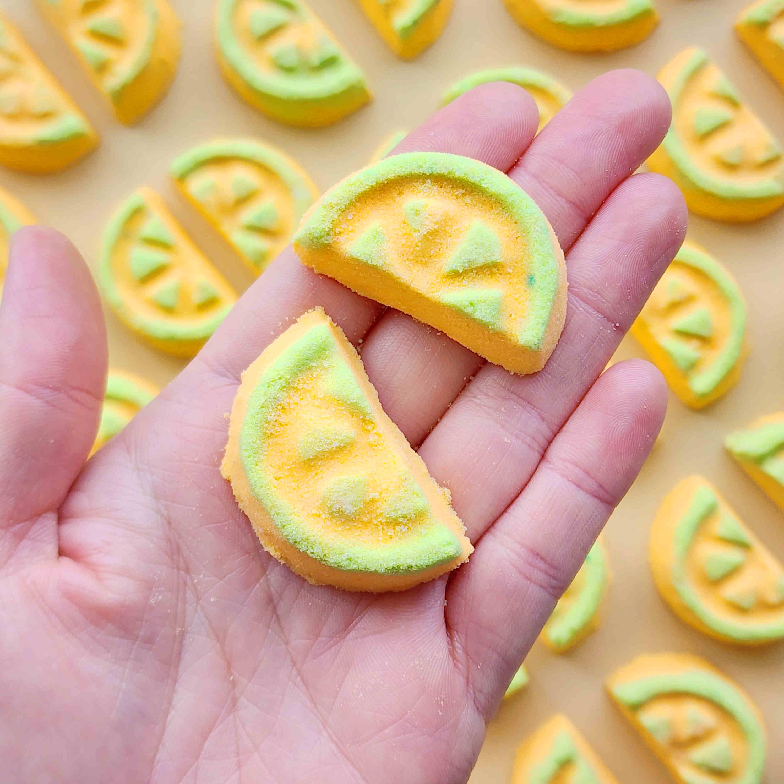Hand holding two honeydew-slice mini bath bombs