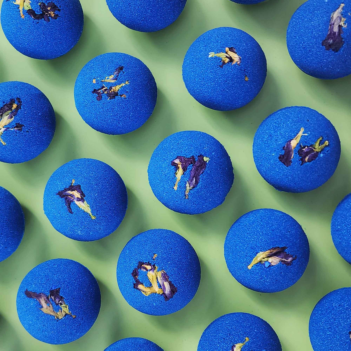 deep blue bath bombs with dried pea flowers on top on a plain green background