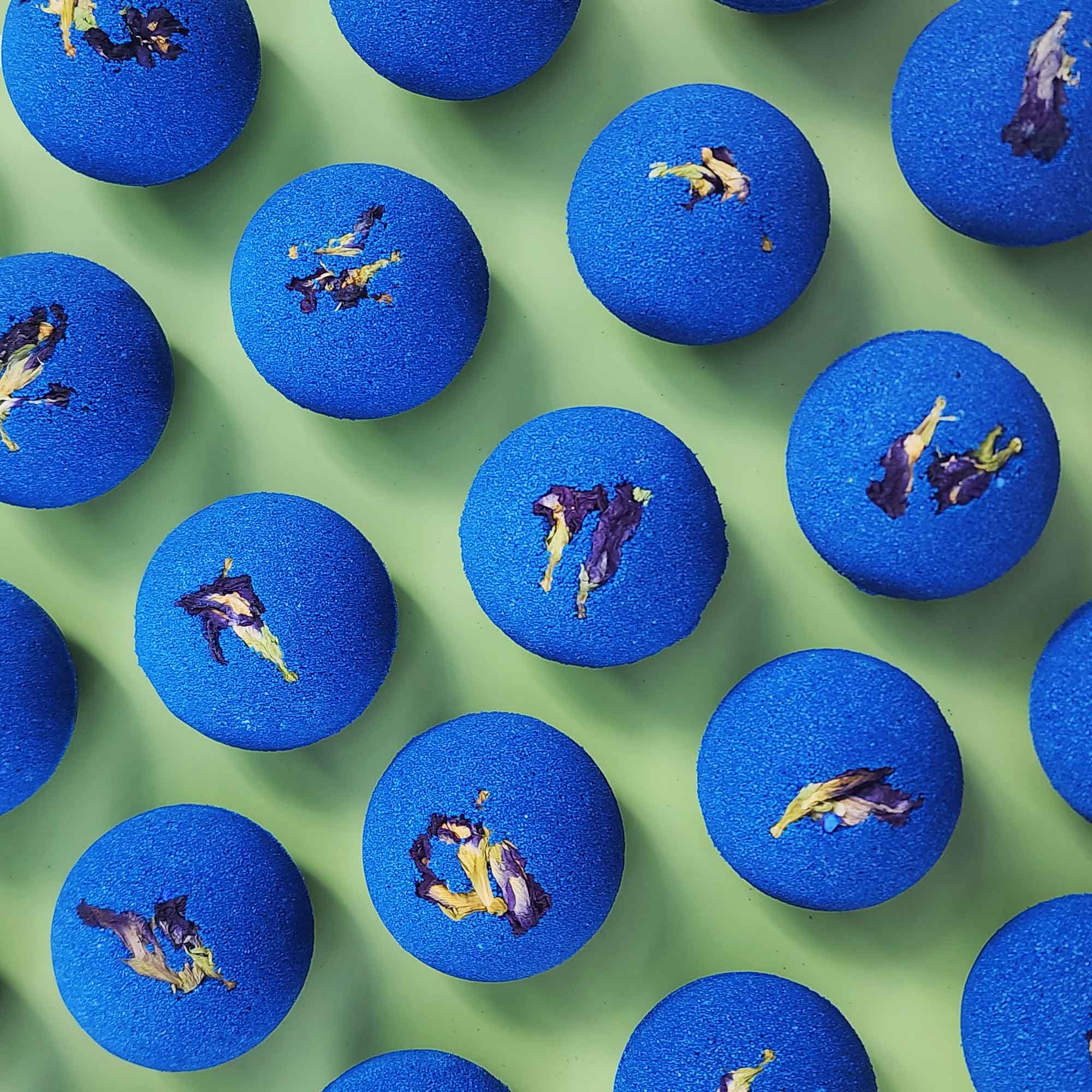 deep blue bath bombs with dried pea flowers on top on a plain green background