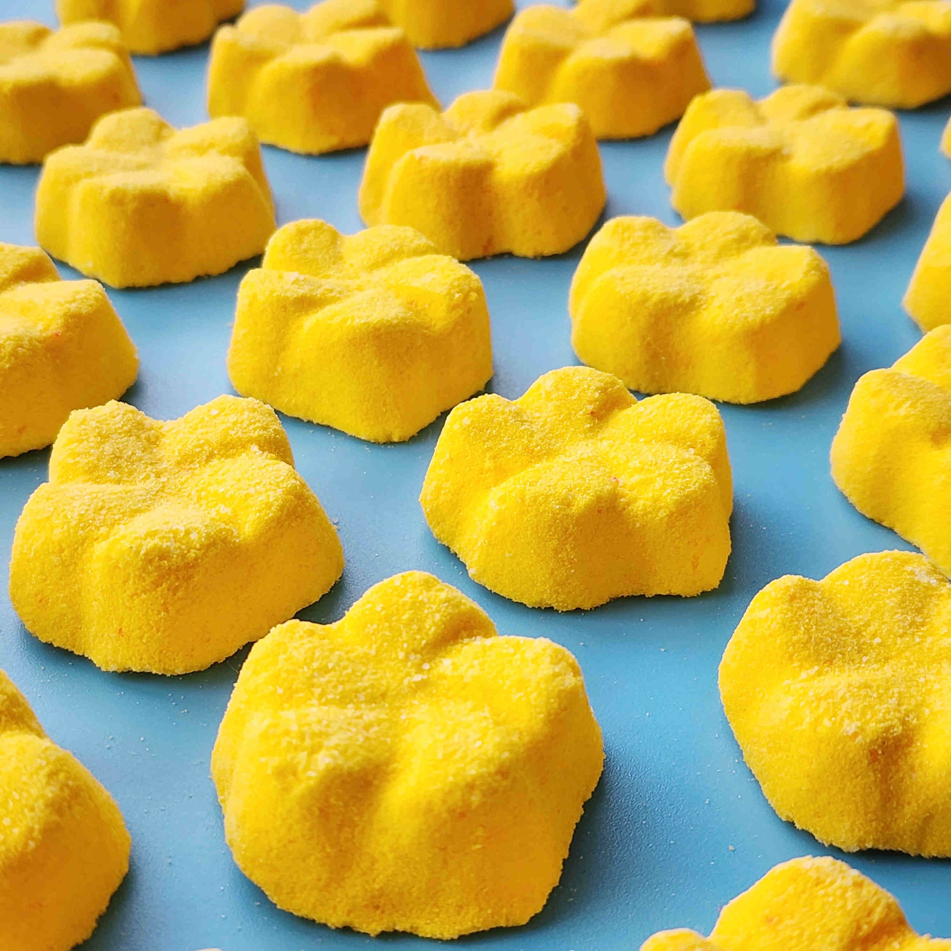 yellow frangipani shaped bath bombs placed in a neat array on a blue background
