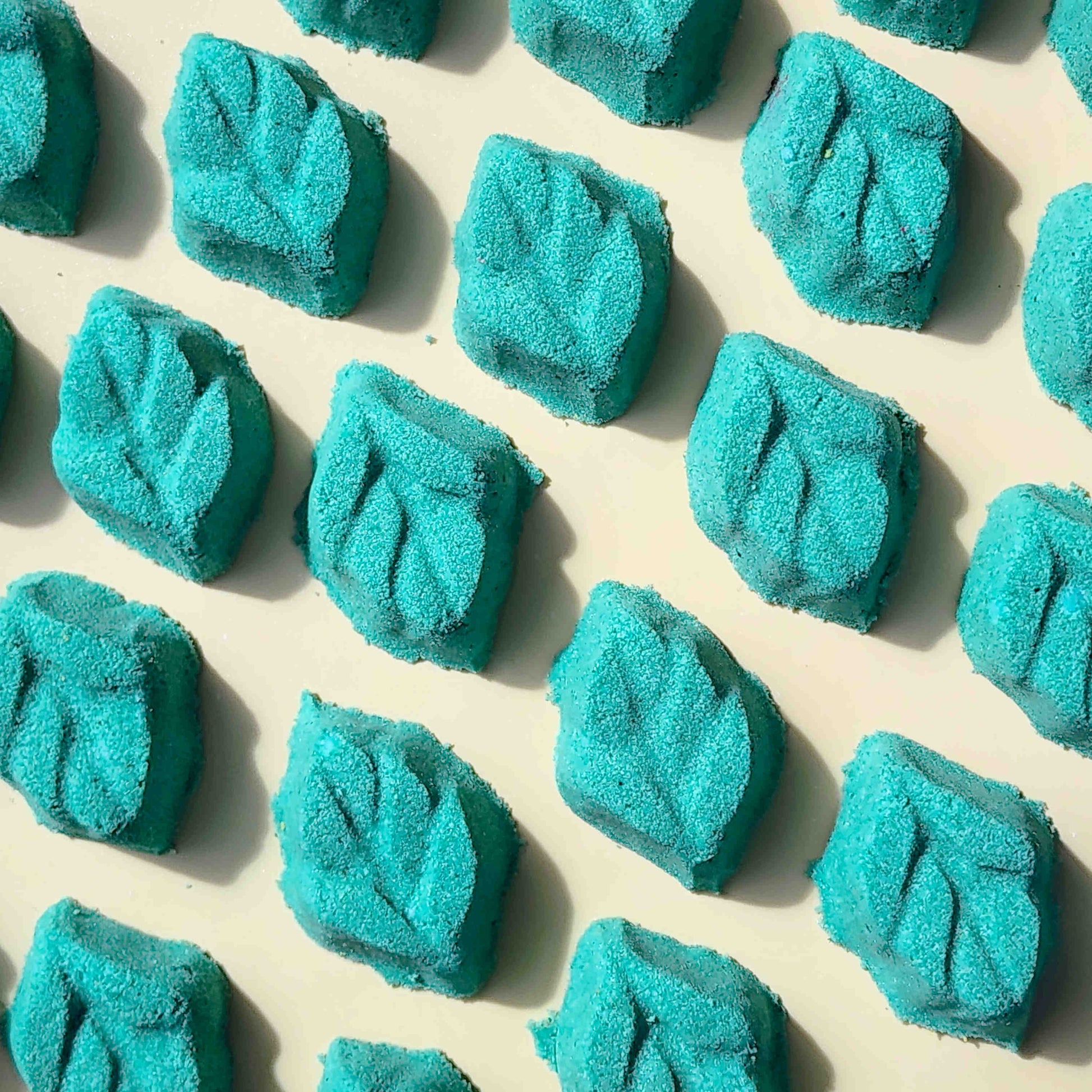 teal leaf shaped mini bath bomb laid out in a neat array over a plain beige background