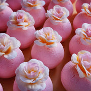 Angled view of pink magnolia bath bombs with white and blush faux petals on a soft background