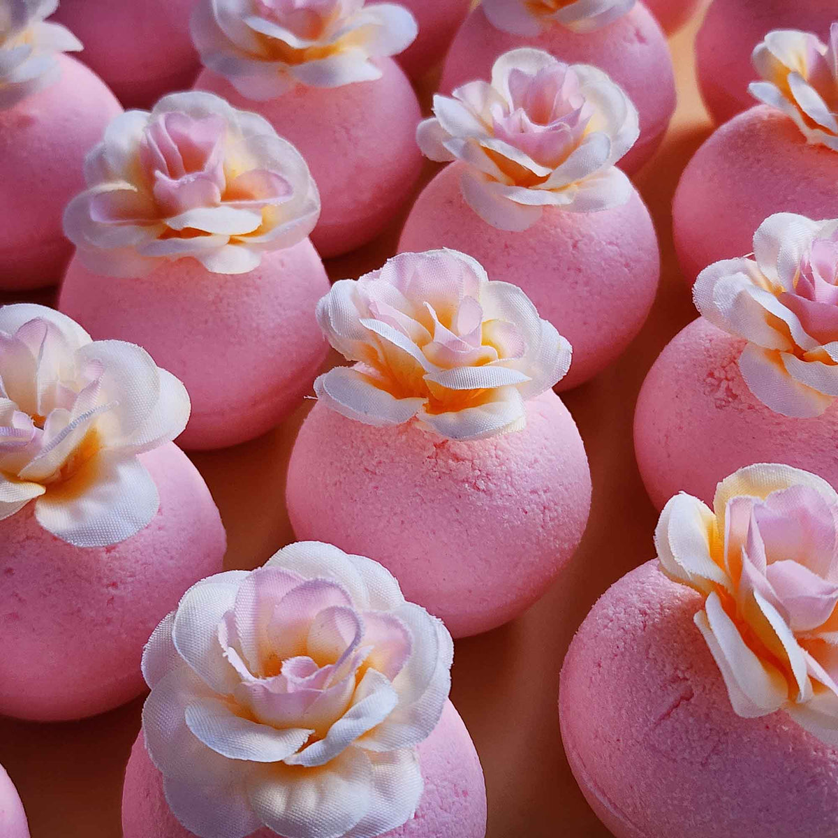 Angled view of pink magnolia bath bombs with white and blush faux petals on a soft background
