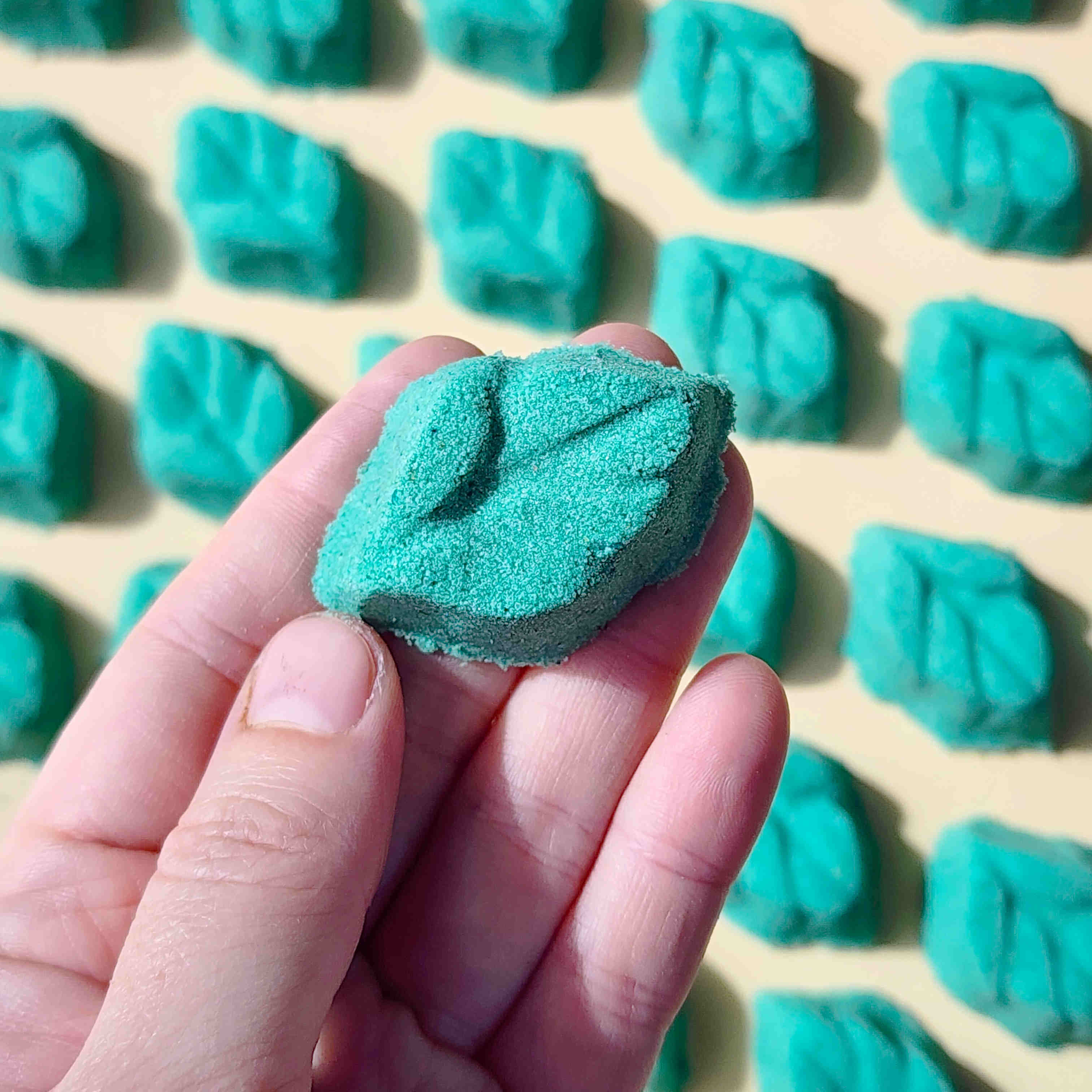 teal leaf shaped mini bath bomb laid out in a neat array over a plain beige background