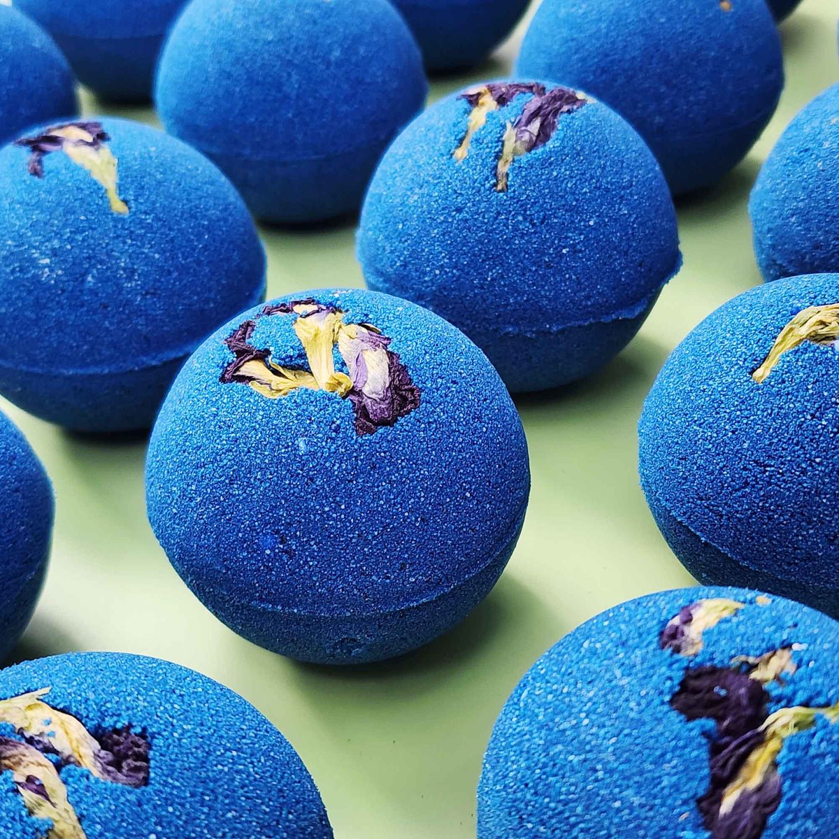 deep blue bath bombs with dried pea flowers on top on a plain green background