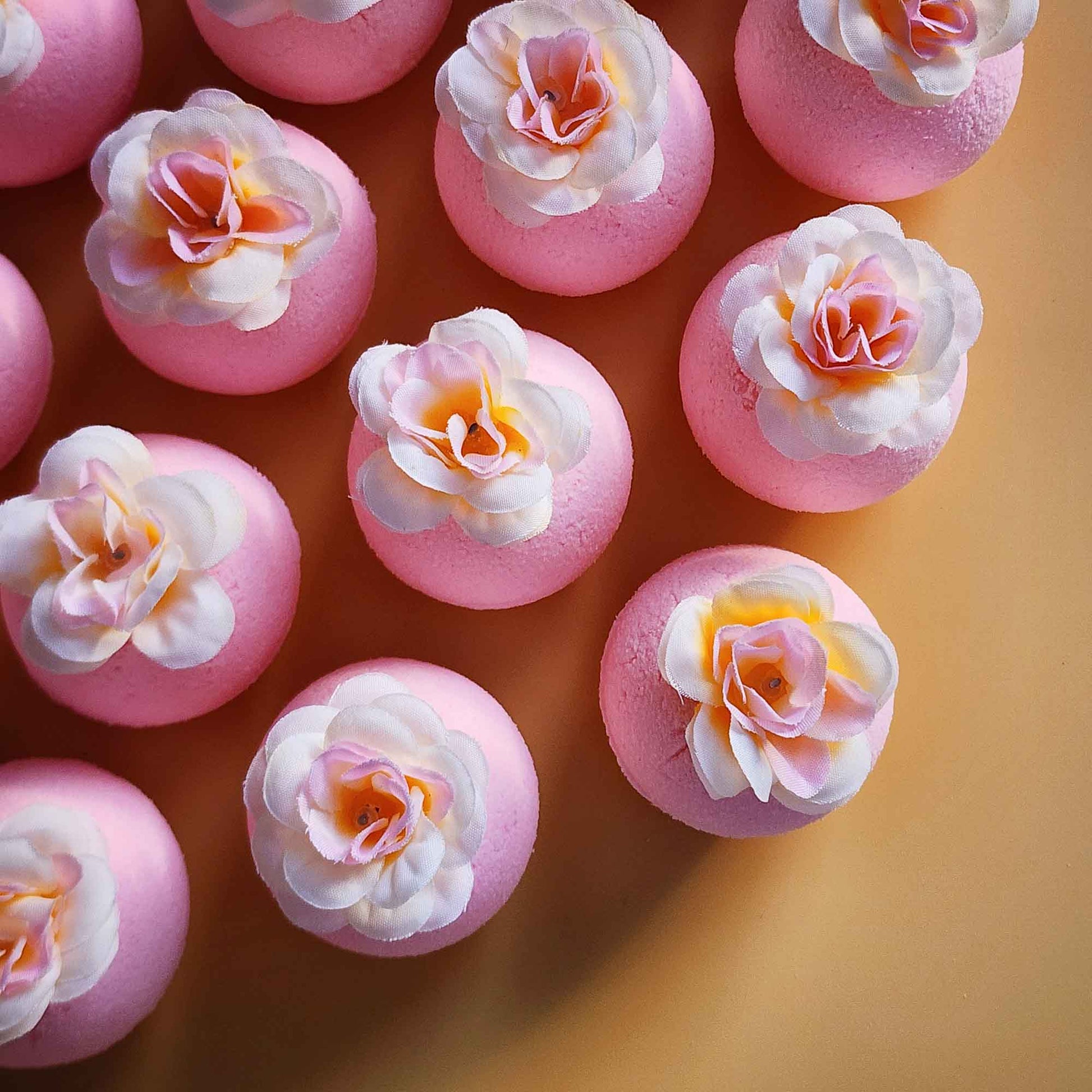 Overhead view of pink magnolia bath bombs arranged together, each finished with a pale fabric flower