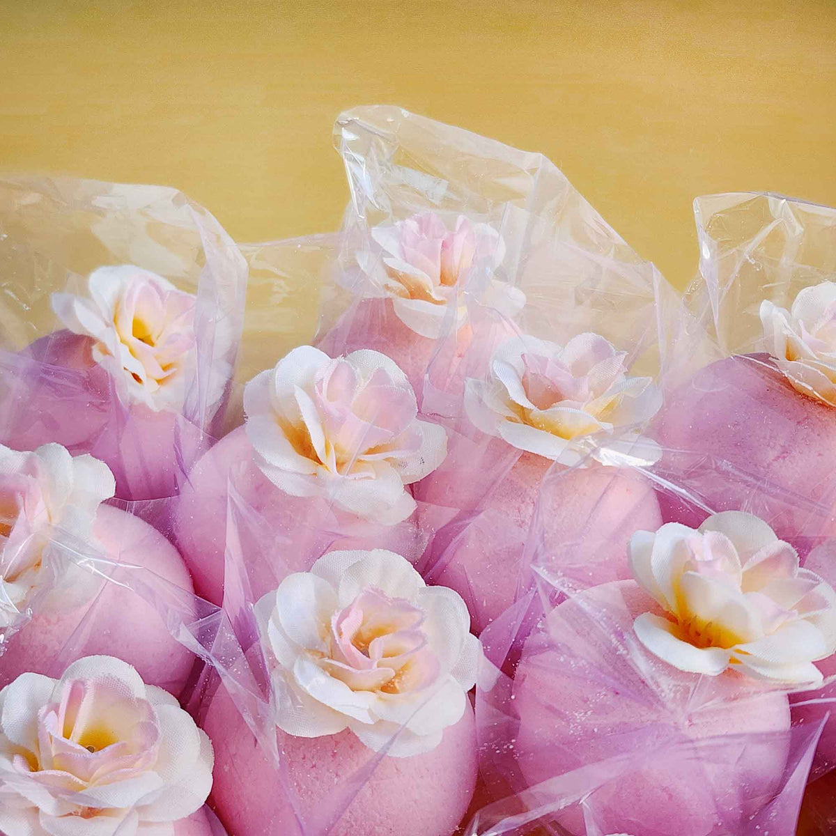 Pink magnolia bath bombs wrapped in clear plastic, each with a delicate faux bloom on top