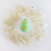Green egg shaped bath bomb with yellow speckles surrounded by light green glow in the dark insect figurines