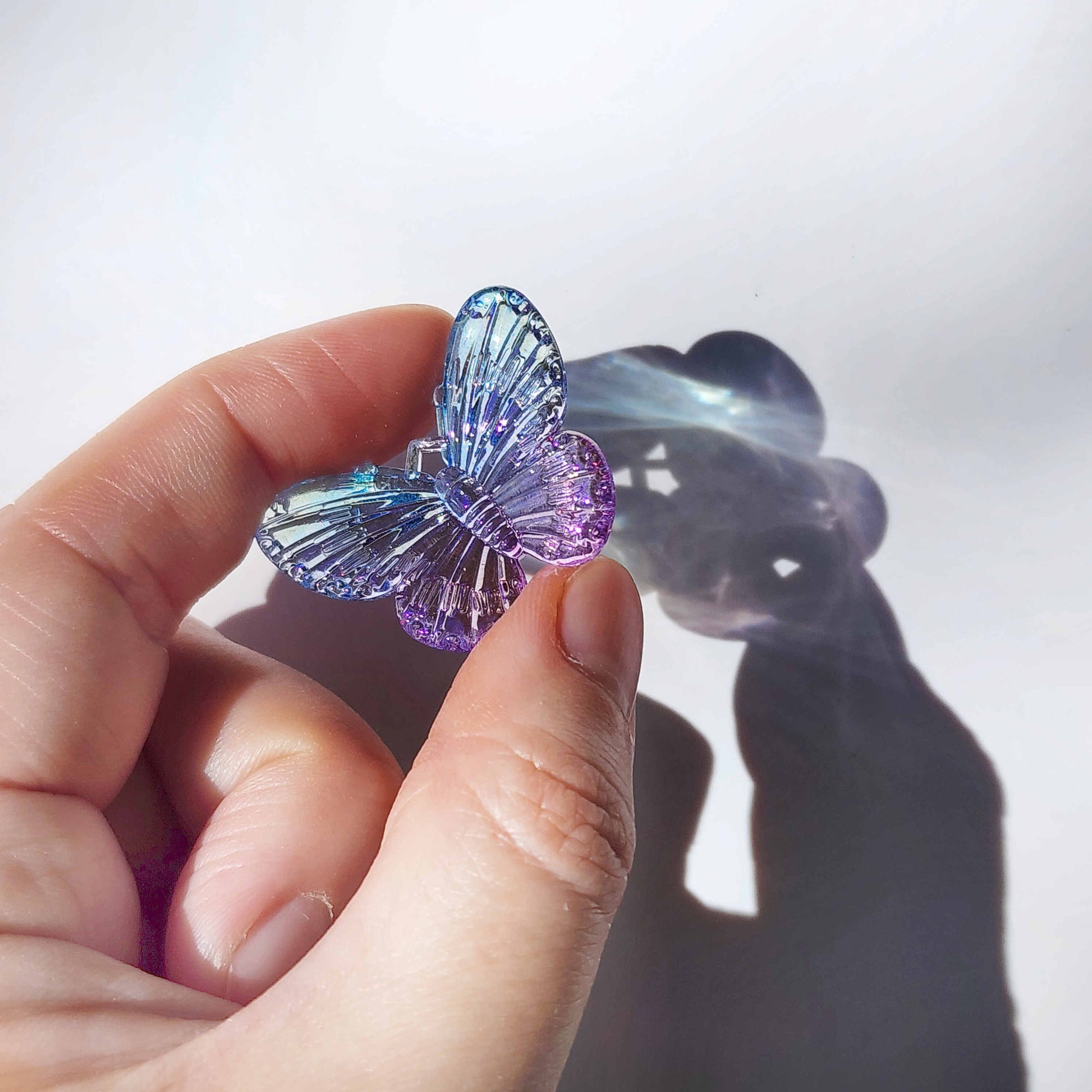 a transparent blue butterfly charm catching sunlight, held between two fingers