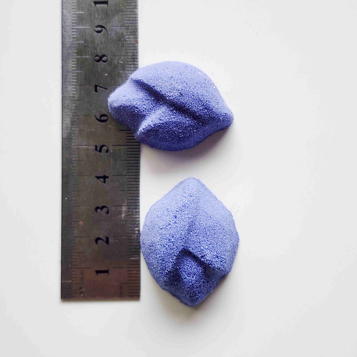 Two lip-shaped Lavender mini bath bombs measured beside a ruler
