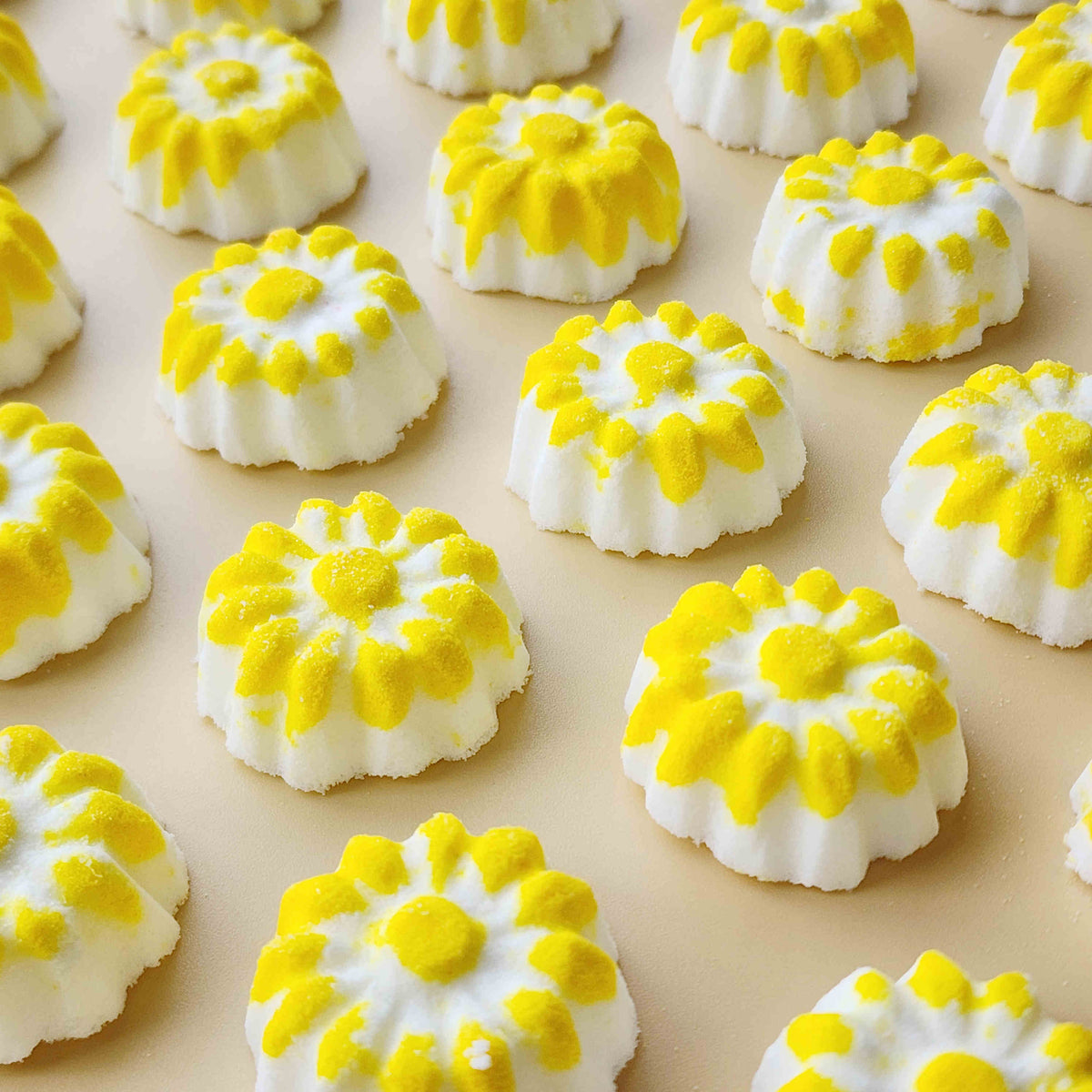 chamomile shaped mini bath bombs with a white base and yellow detail on a neutral plain background