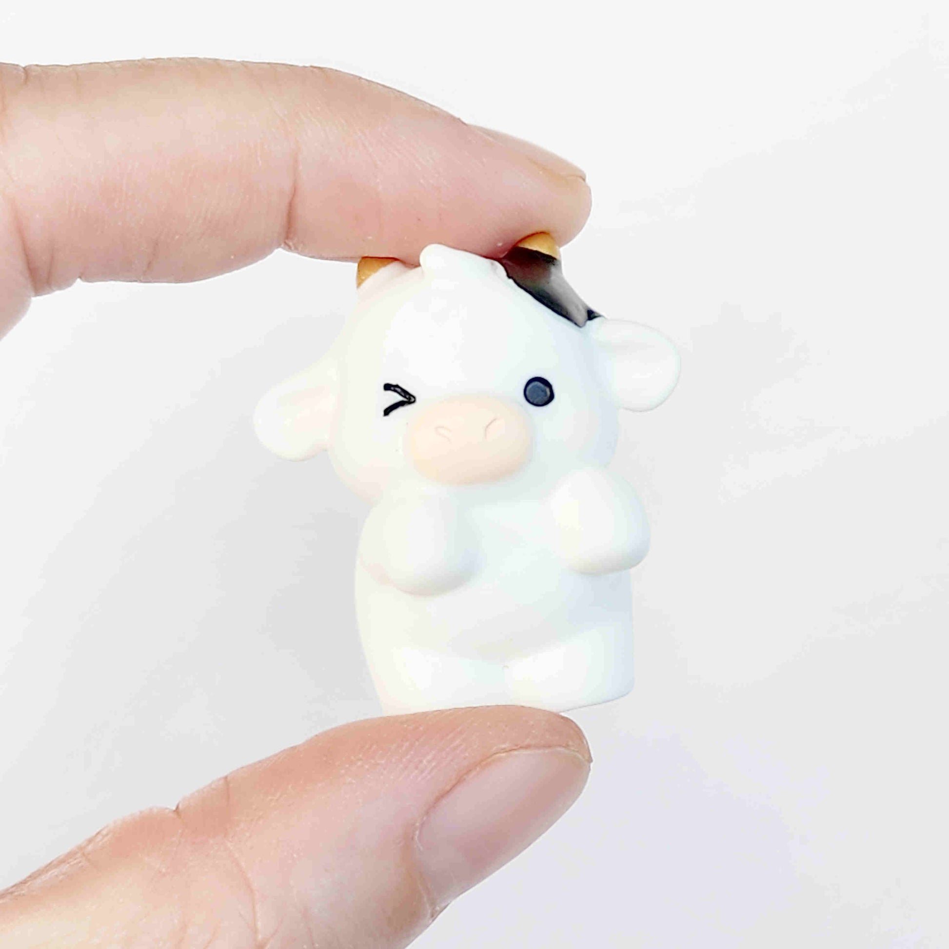 cute cow figurine with gold horns on a white background being held between two fingers