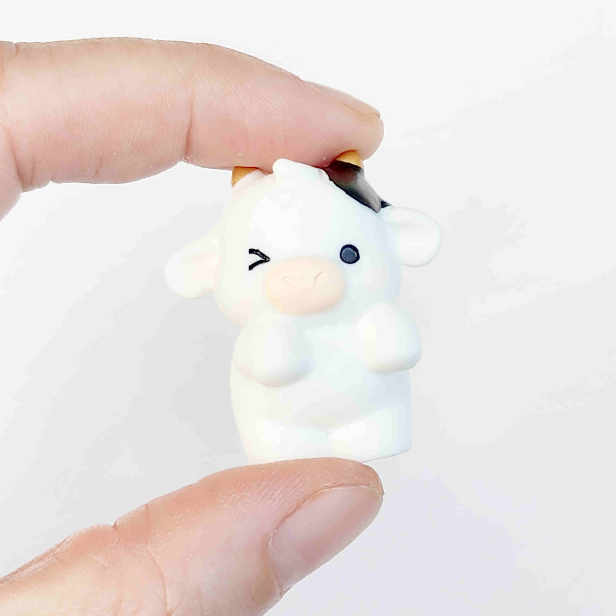 cute cow figurine with gold horns on a white background being held between two fingers