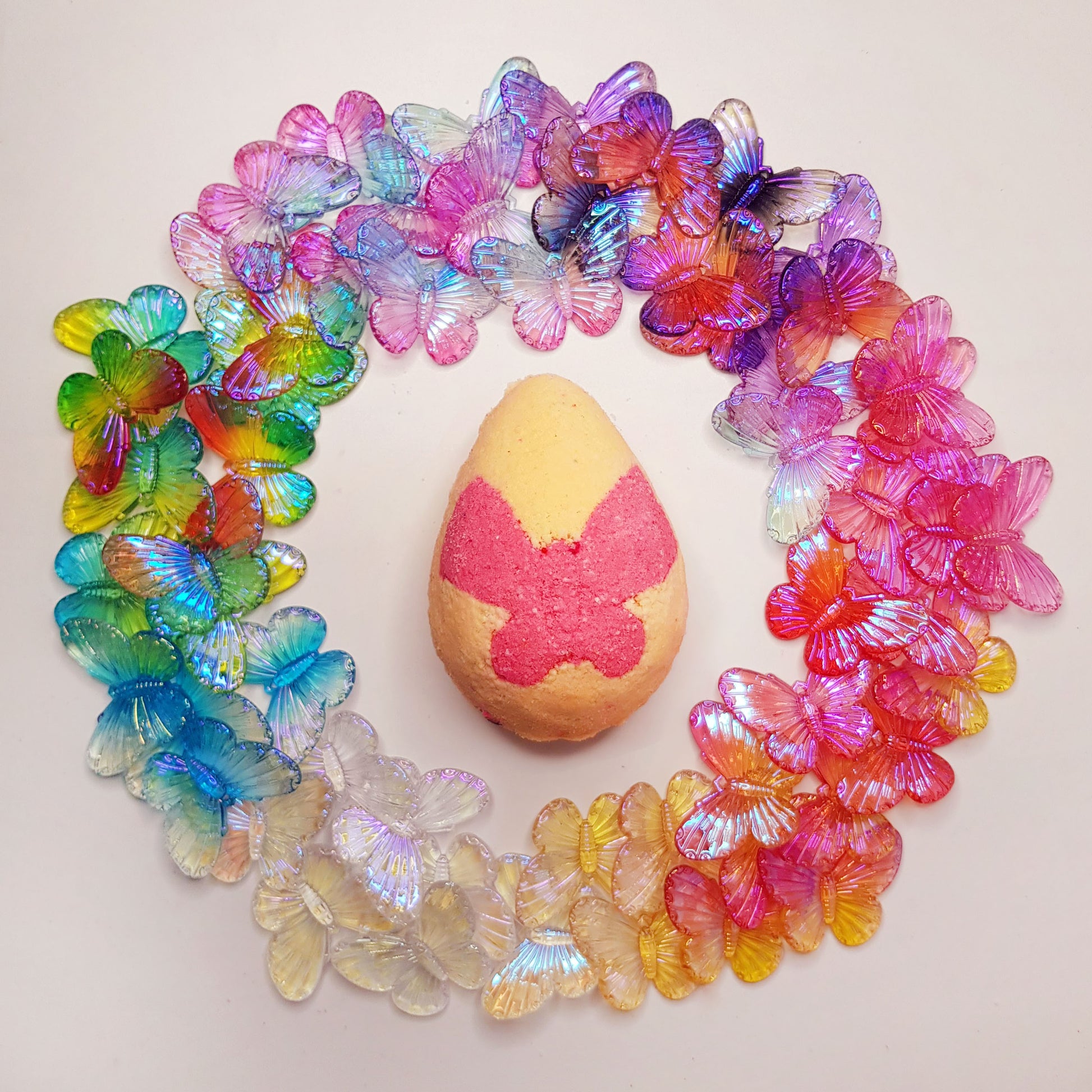 peach egg shaped bath bomb with a bright pink butterfly in the middle surrounded by vibrant translucent butterfly charms