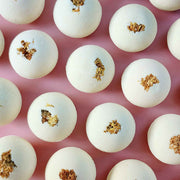 Cream white round essential oil aromatherapy bath bombs with dried chrysanthemum on a plain pink background