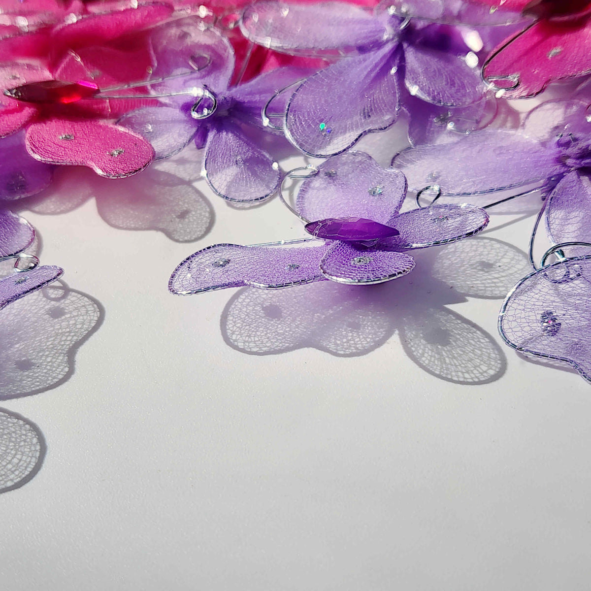 scattered pink and purple butterflies made of mesh fabric and wire on a white background