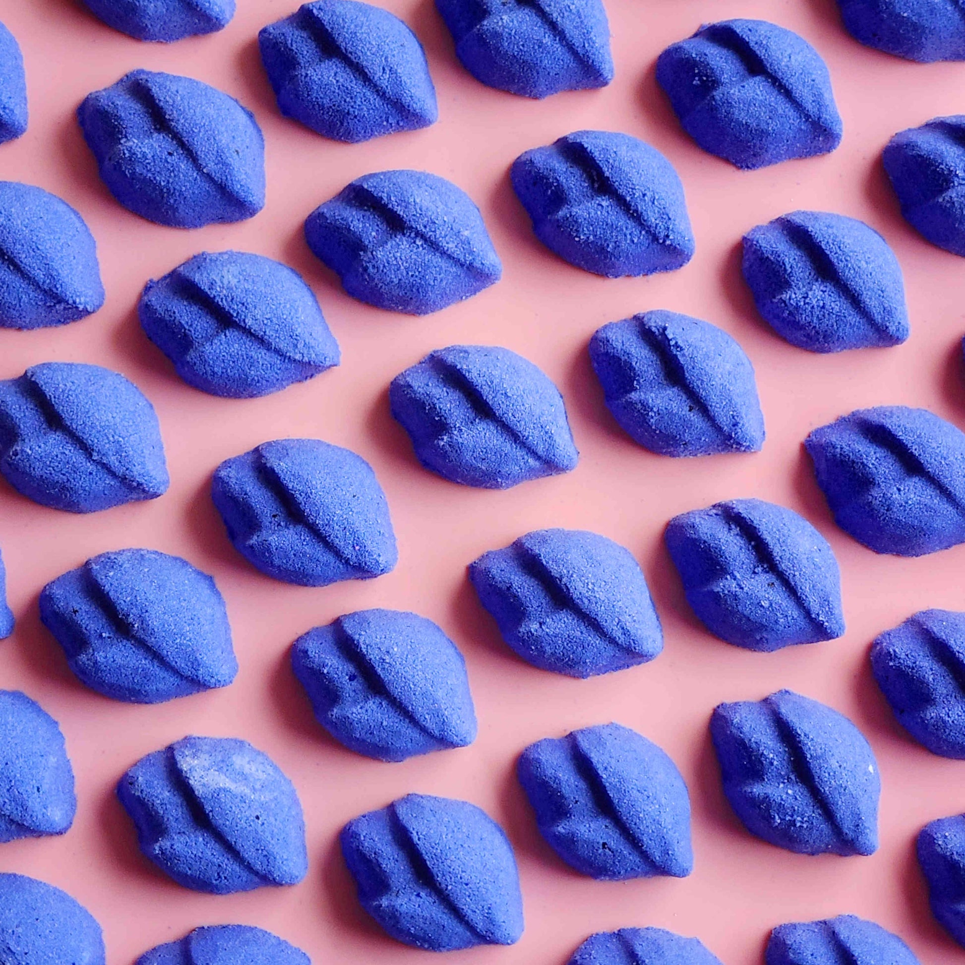 Rows of purple lip-shaped Lavender mini bath bombs on a pink background