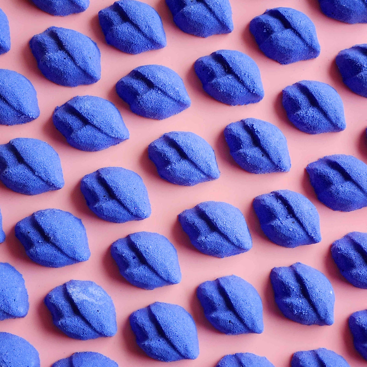 Rows of purple lip-shaped Lavender mini bath bombs on a pink background