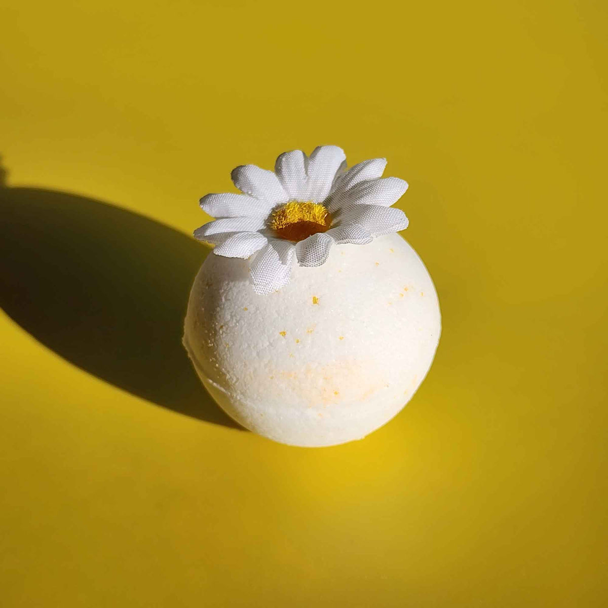 White chamomile bath bomb topped with a faux daisy flower on a bright yellow background