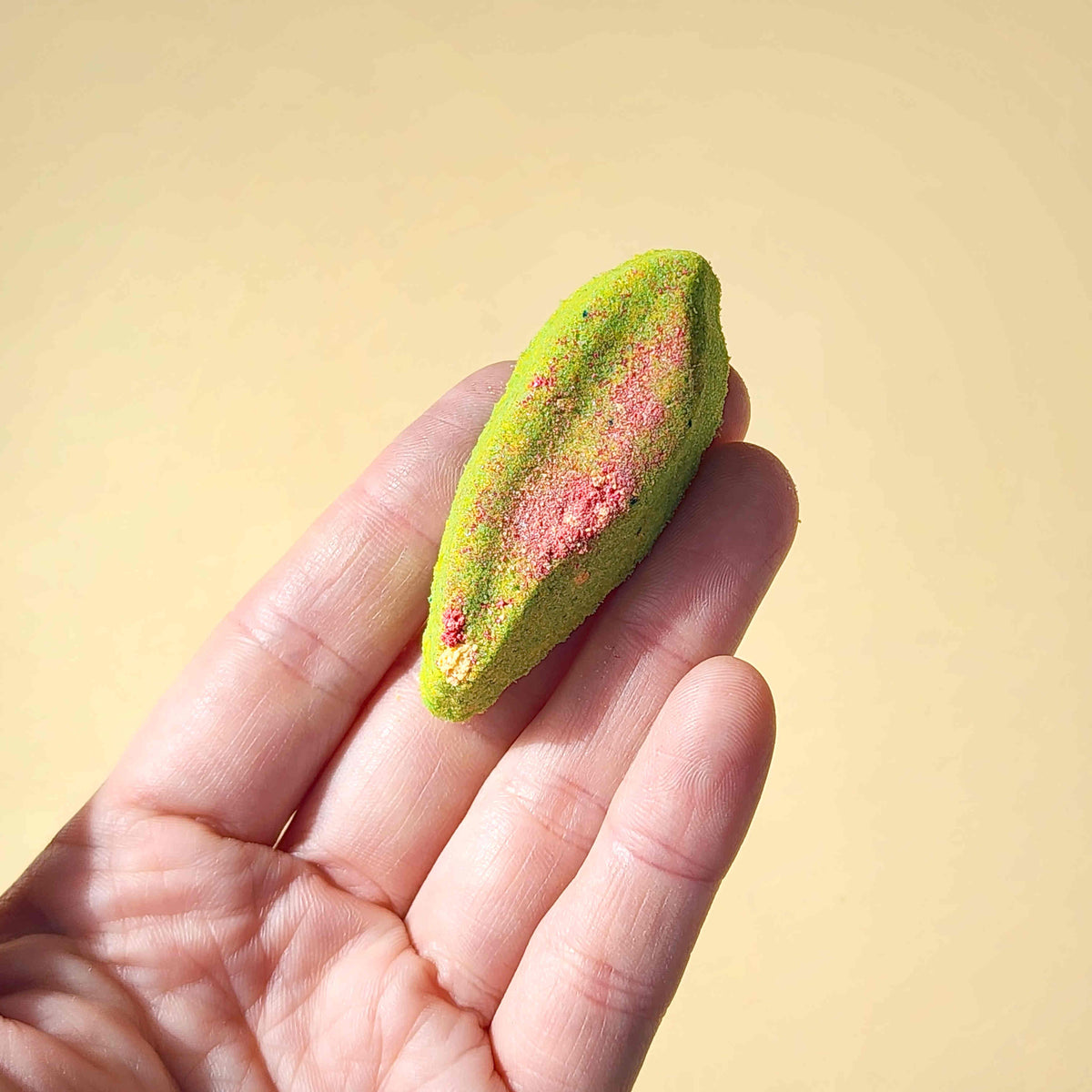 Long eucalyptus leaf shaped bath bomb being held in a hand on a plain beige background