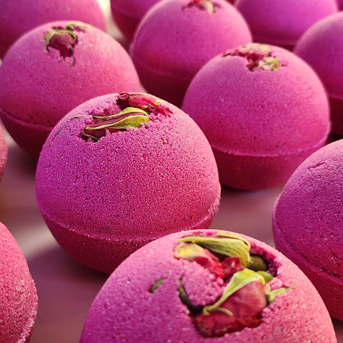 velvet red round aromatherapy bath bombs with dried rose buds on a dusty pink background