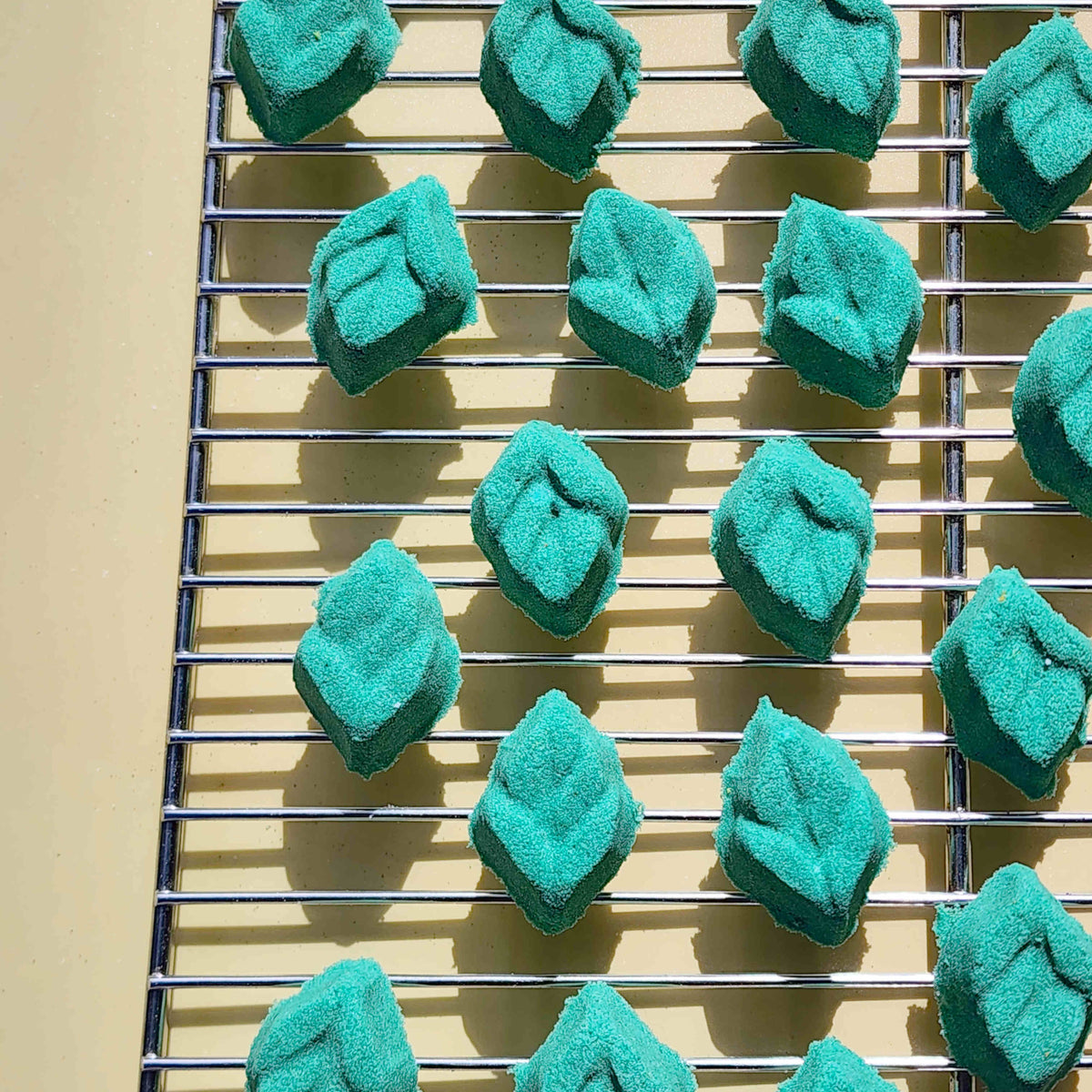 teal leaf shaped mini bath bomb laid out in a neat array over a plain beige background