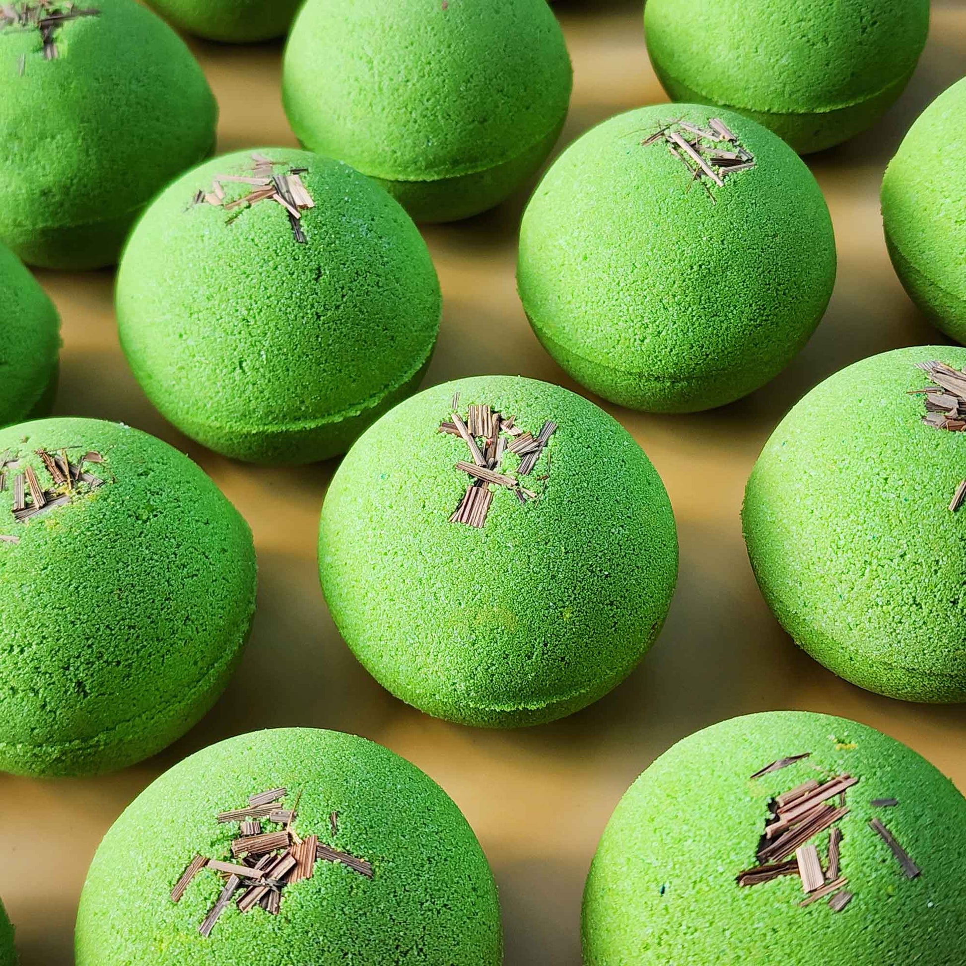 Multiple bright green Repair aromatherapy bath bombs topped with small pieces of dried lemongrass on a warm yellow background
