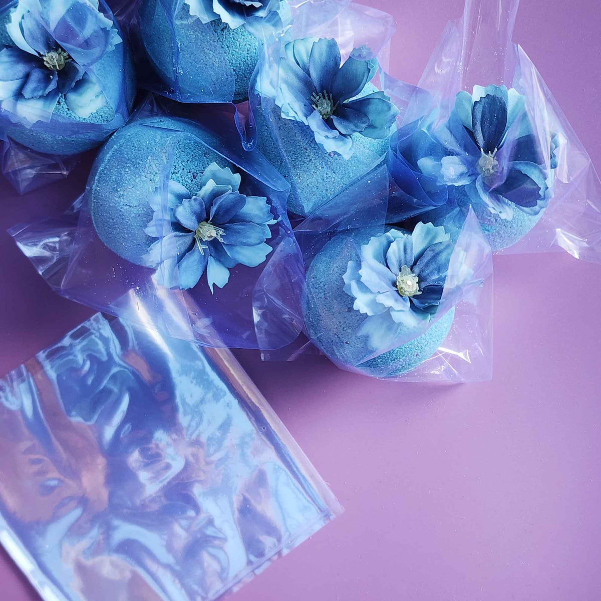 Blue floral bath bombs individually wrapped in clear plastic, their soft blue flowers visible through the packaging