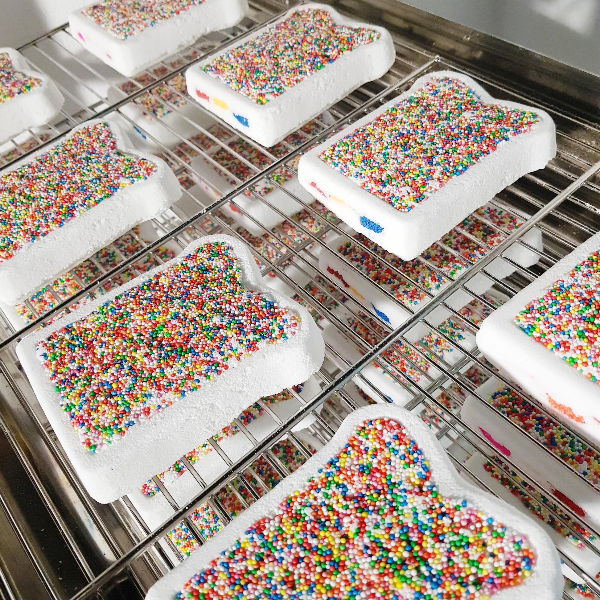 Fairy Bread bath bombs covered in rainbow sprinkles on cooling racks