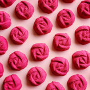 rose shaped mini bath bombs coloured a deep red laid out neatly on a plain pink background