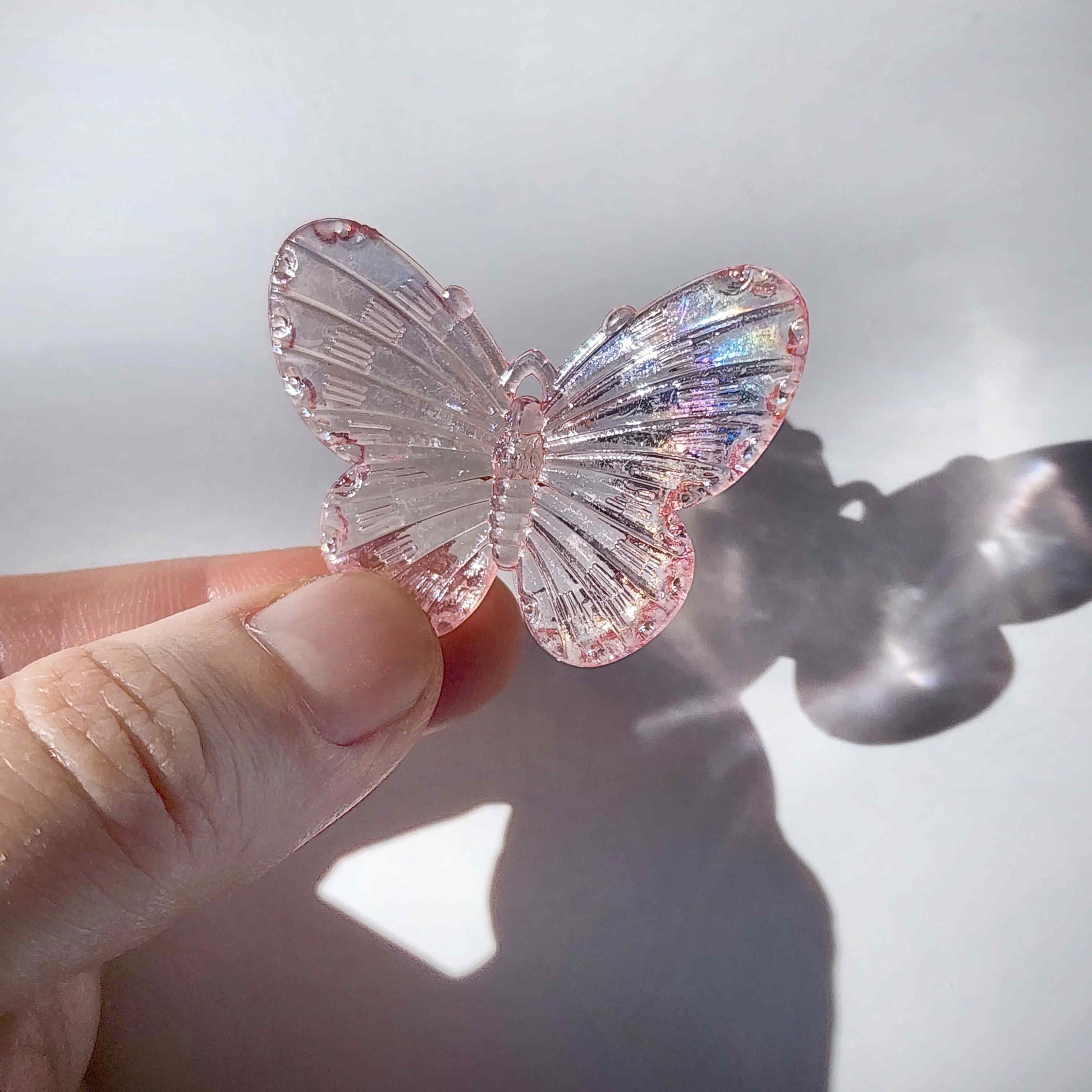 pink transparent butterfly charm being held by two fingers on a white background