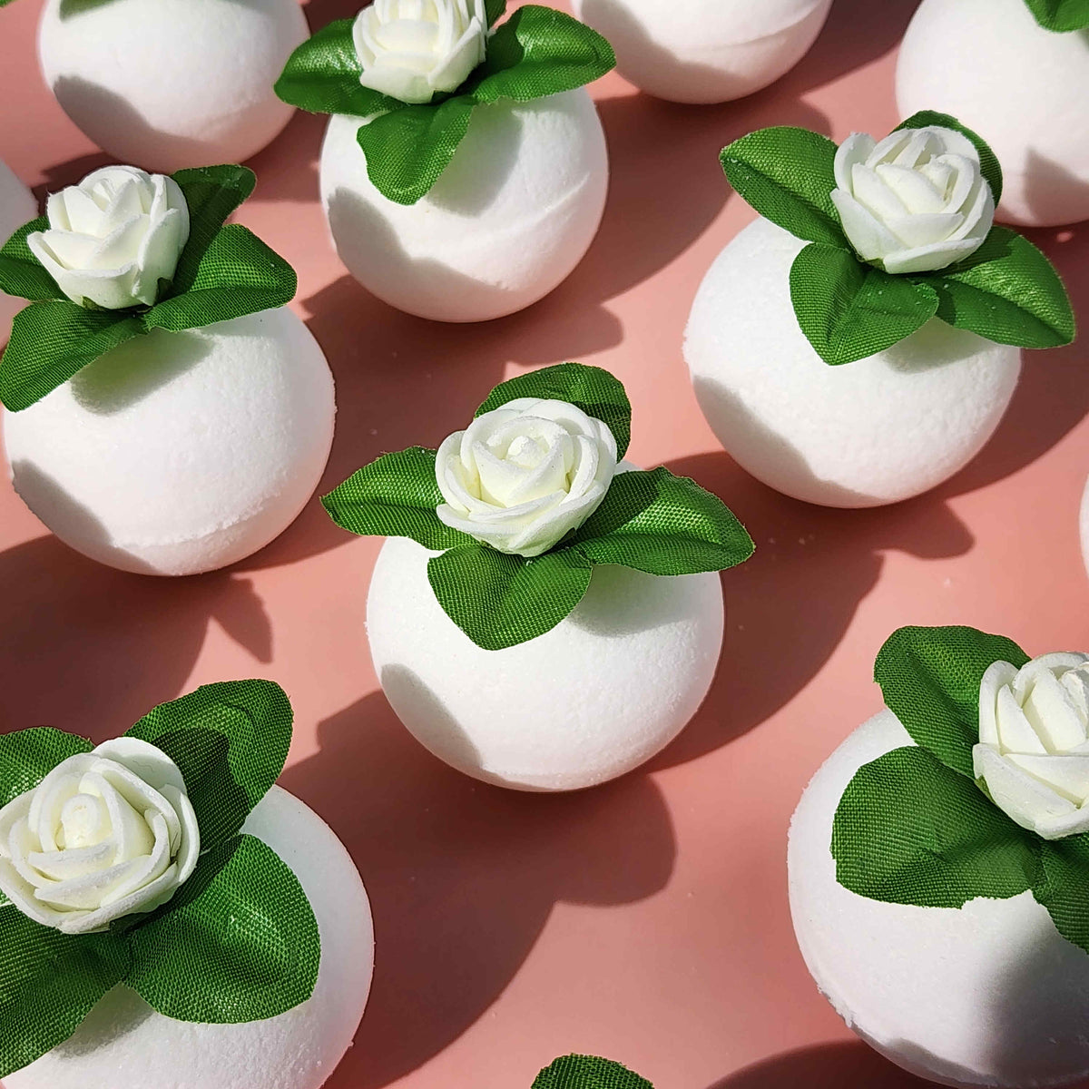 round white bath bombs with jasmine flowers on top over a pink background
