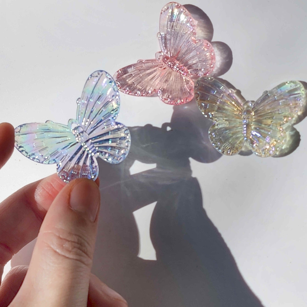 blue transparent acrylic butterfly charm being held up in front of a pink and yellow butterfly charm on a white background