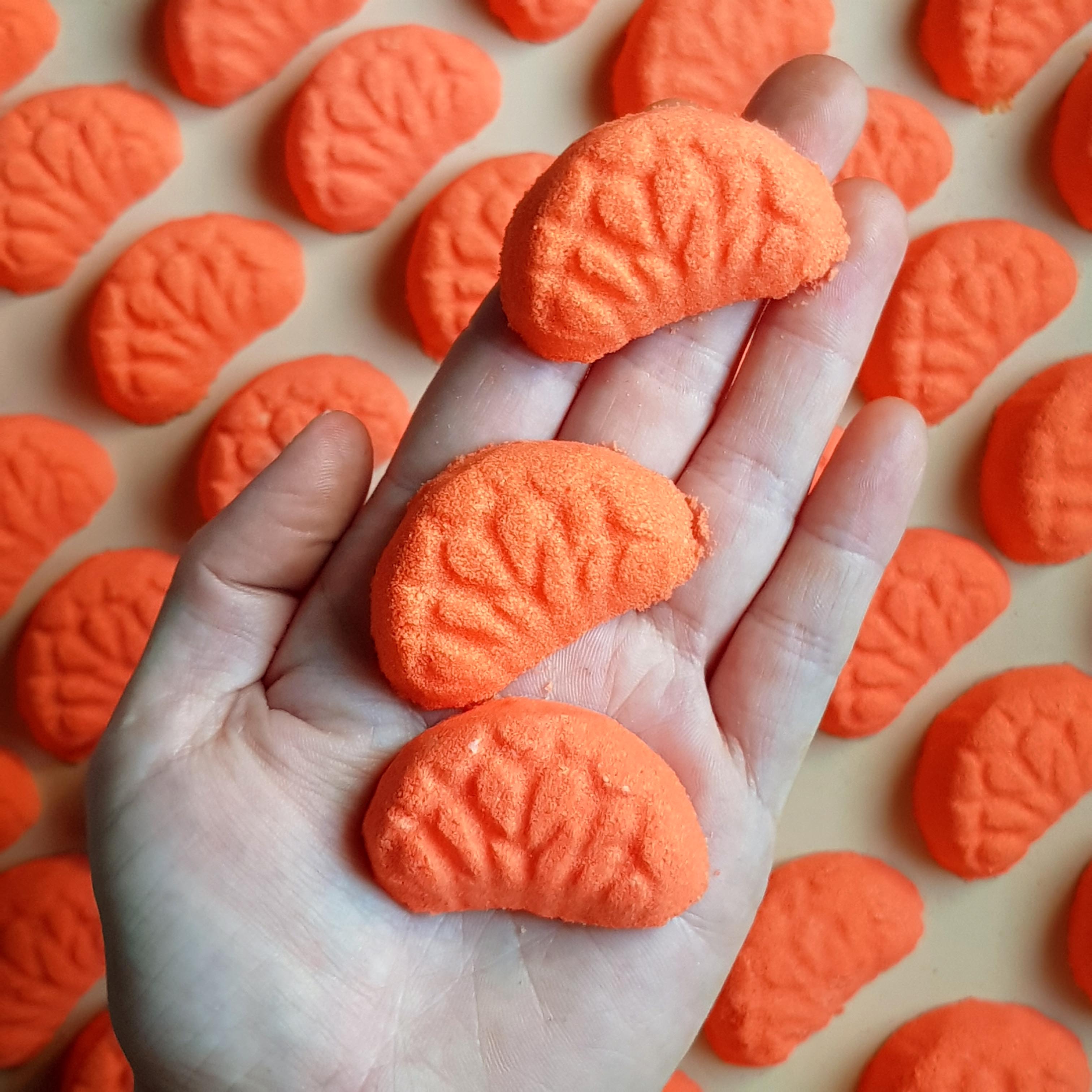 Miniature vibrant orange coloured mandarin bath bombs shaped as mini mandarin slices