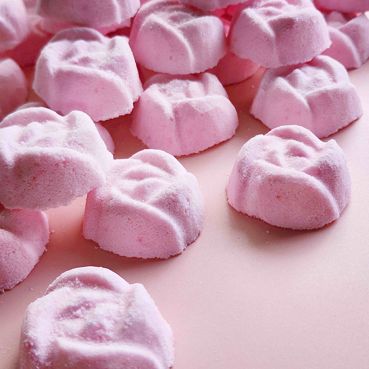 light dusty pink coloured mini bath bombs in the shape of roses laid out neatly on a plain pink background