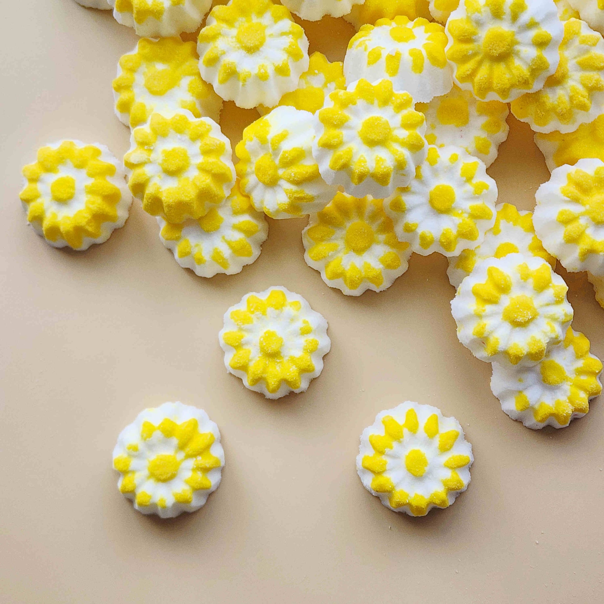chamomile shaped mini bath bombs with a white base and yellow detail on a neutral plain background