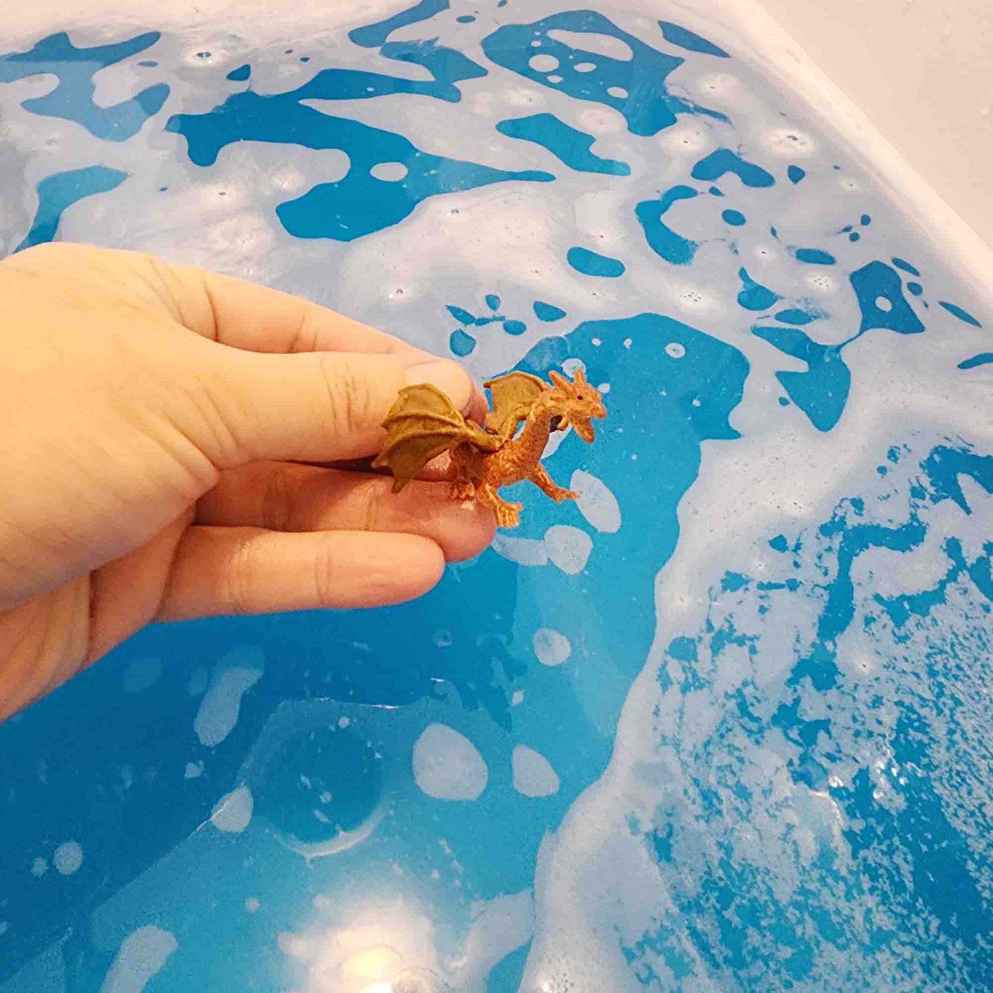 Brown dragon toy being held in a hand over a bathtub filled with bright blue water
