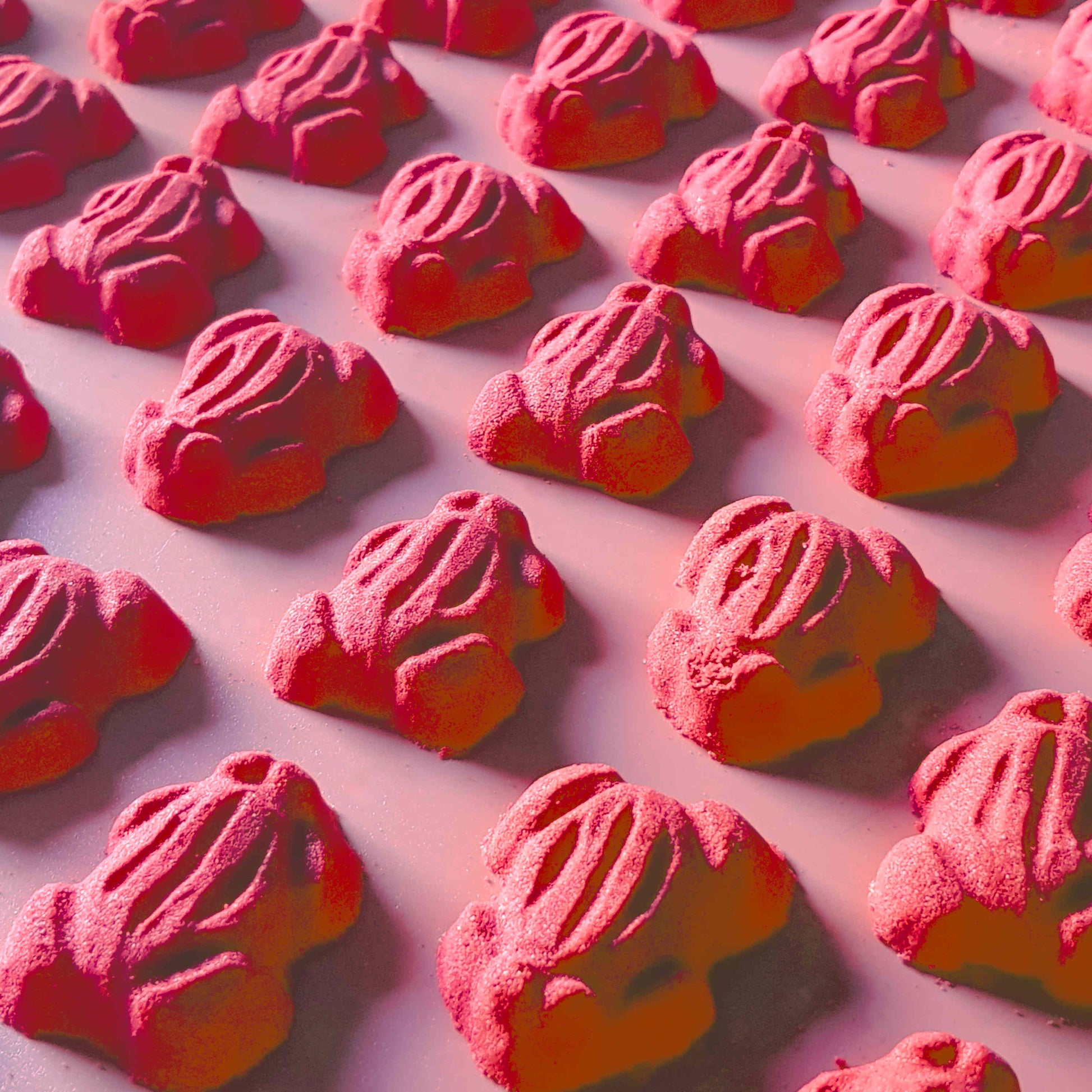 Red frog gummy candy shaped bath bombs layed out in an array over a plain red background
