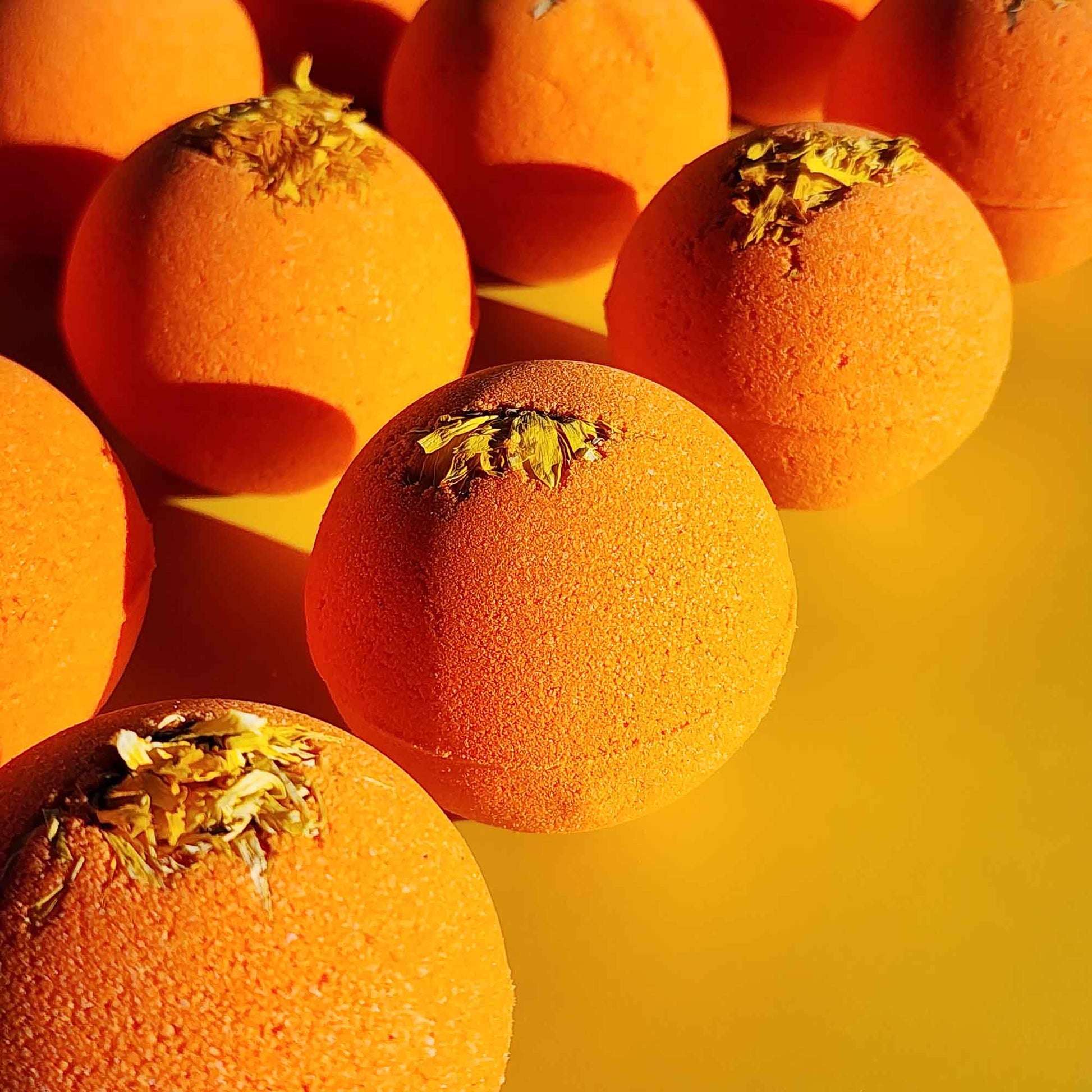 right orange Restore aromatherapy bath bombs topped with whole chrysanthemum flowers on a yellow surface