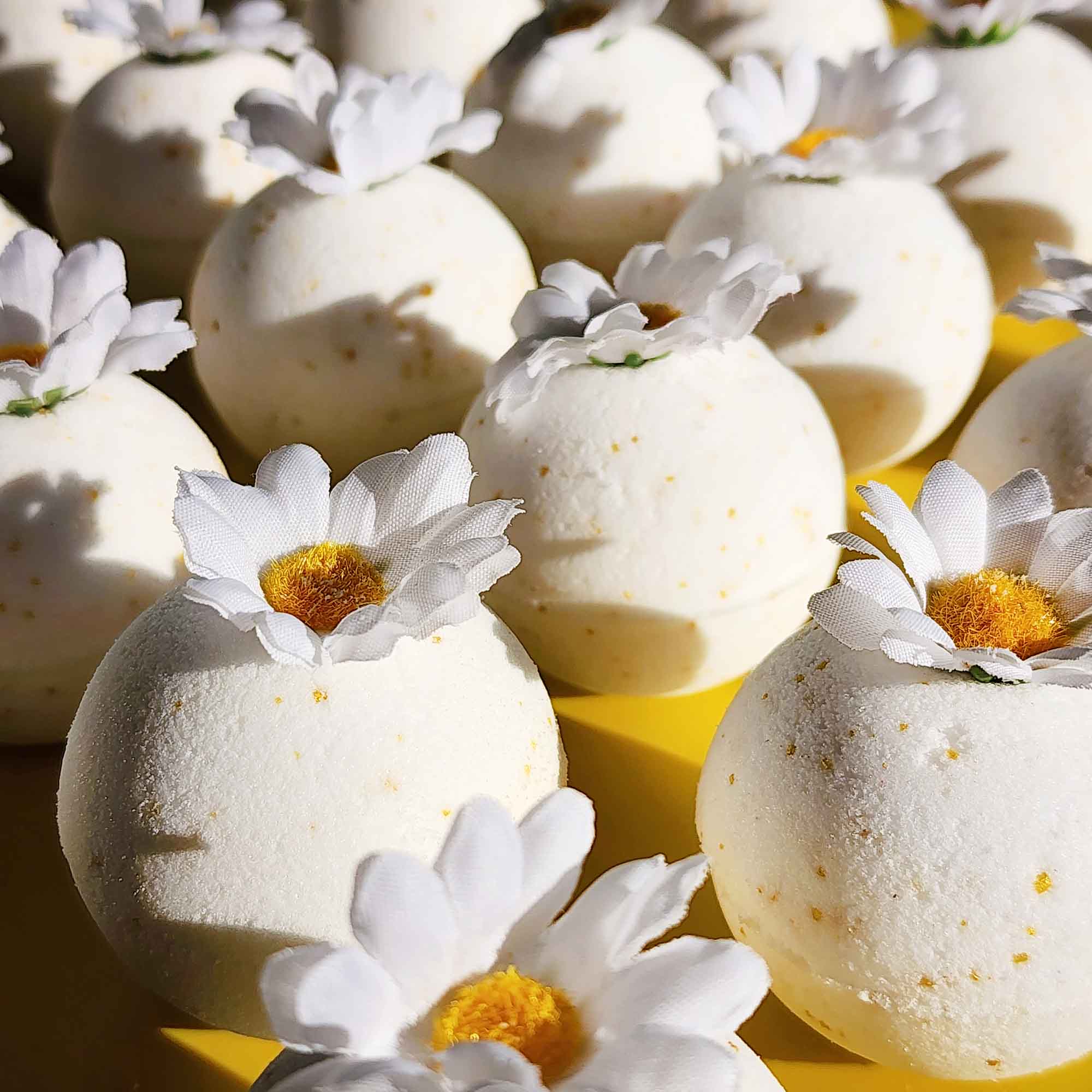 Angled view of white chamomile bath bombs with faux daisies and golden flecks under warm light