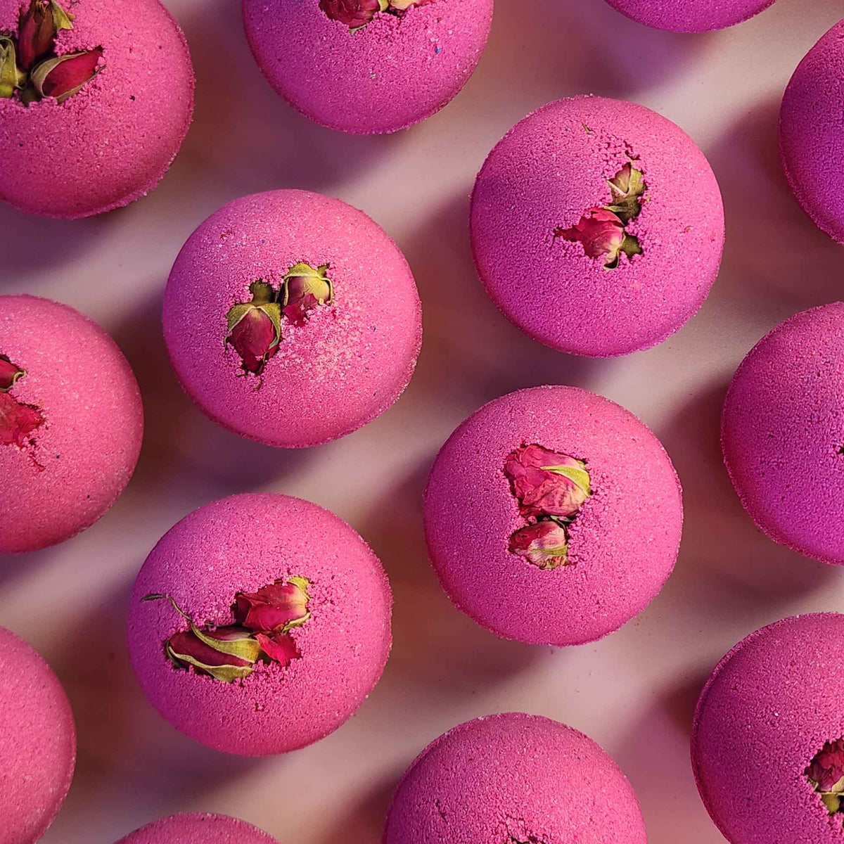 velvet red round aromatherapy bath bombs with dried rose buds on a dusty pink background