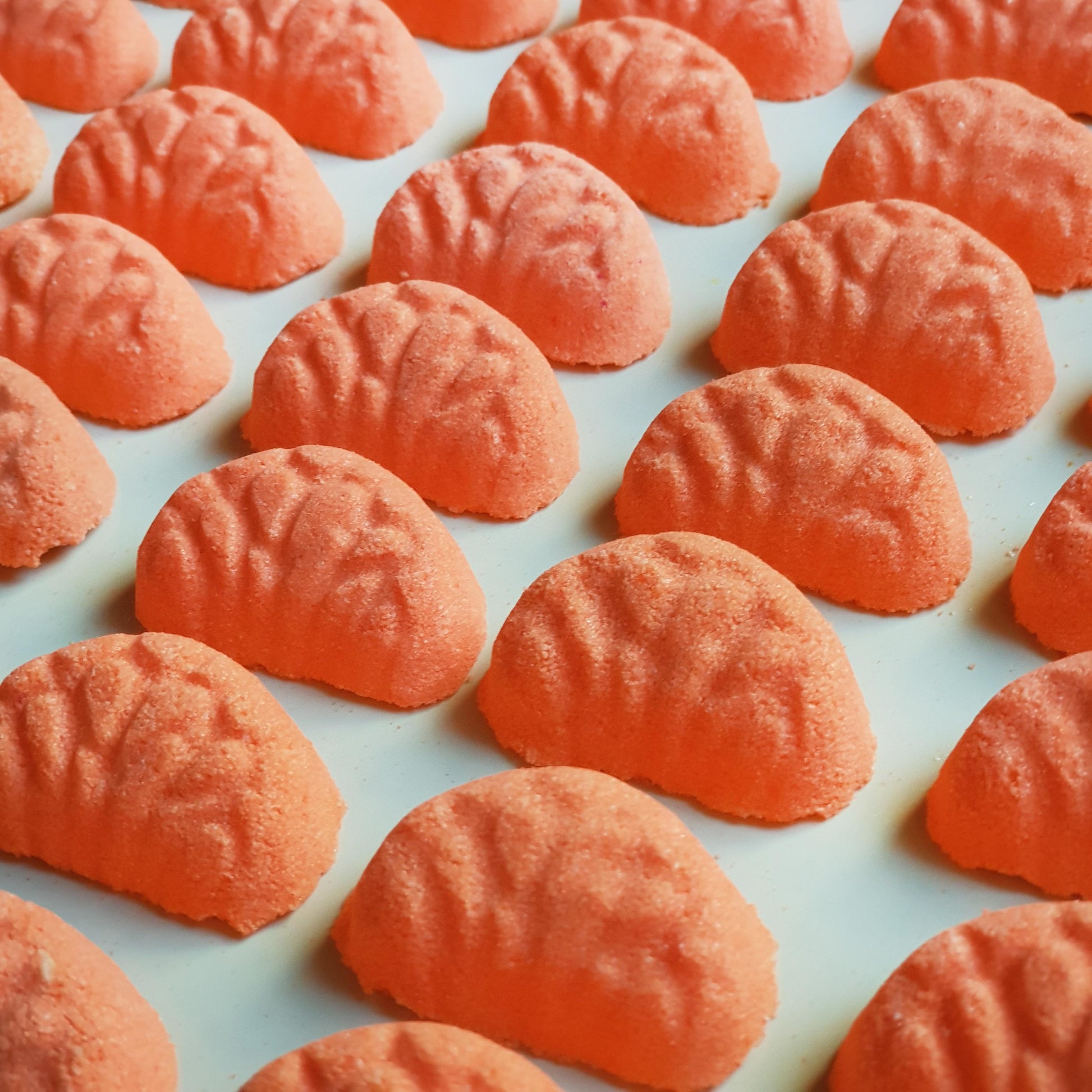 Miniature vibrant orange coloured mandarin bath bombs shaped as mini mandarin slices