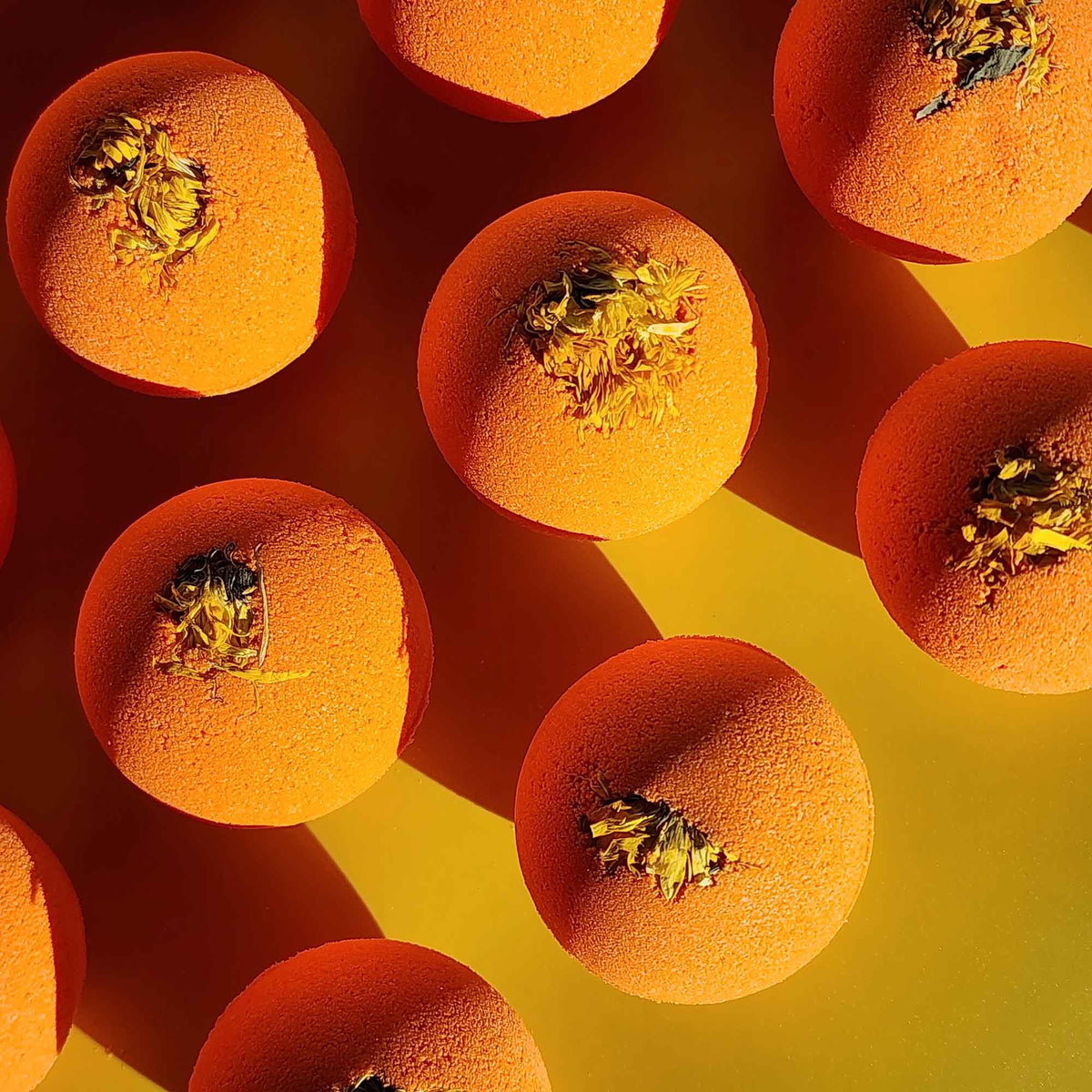 Top-down view of multiple bright orange Restore aromatherapy bath bombs topped with whole dried chrysanthemum flowers