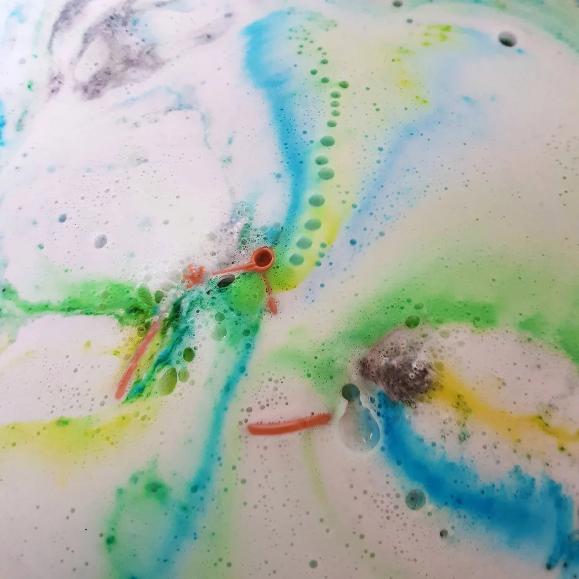 bath bomb foaming and dissolving releasing blue, yellow, and green streaks of colour